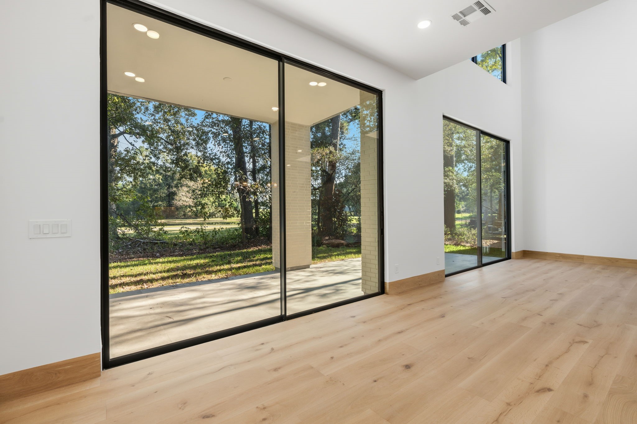 Sunlit living area boasting soaring double-height ceilings  and sliding glass doors that frame picturesque golf course views.