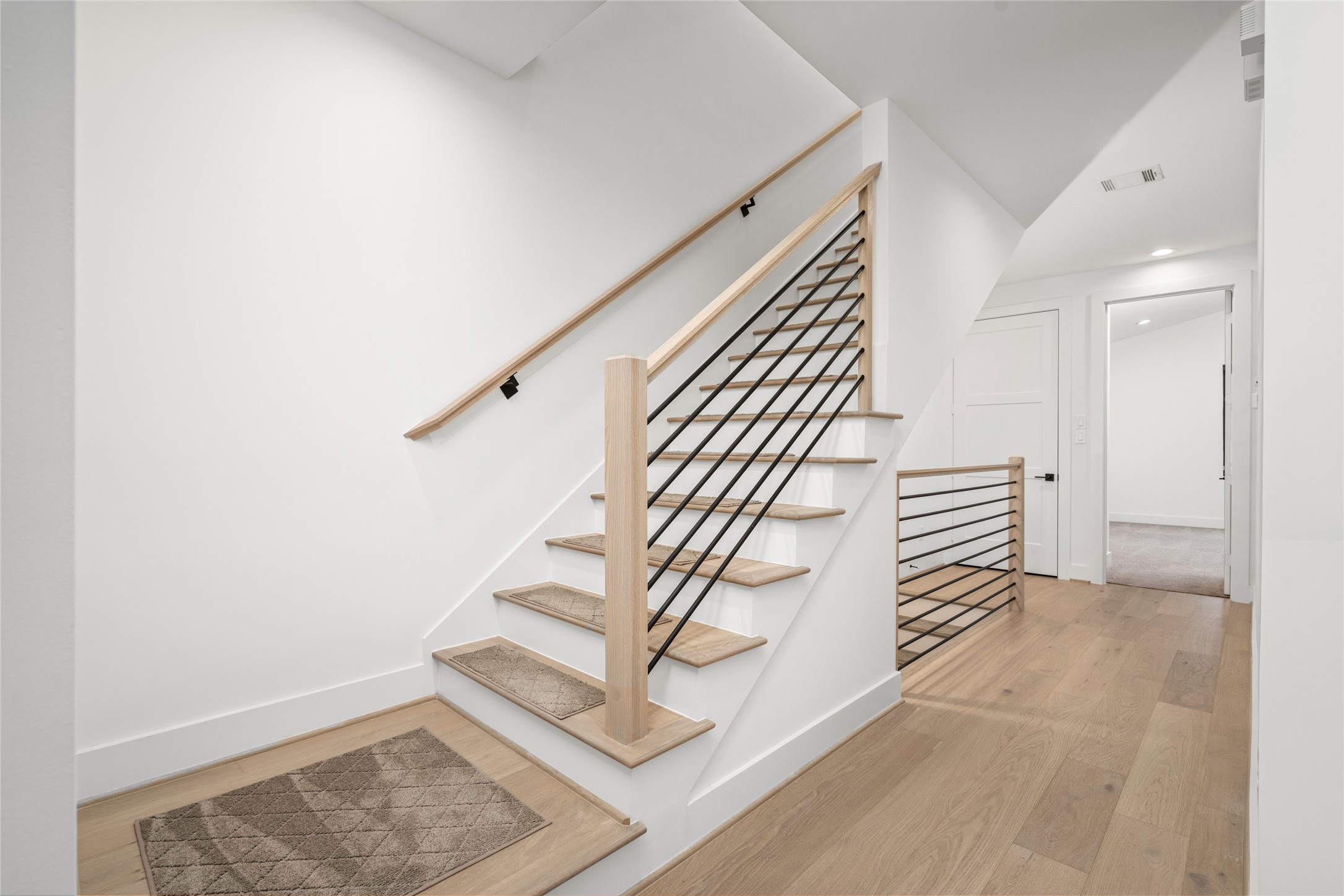 A view of the staircase between the second and third floors.  Transitional iron balusters, wood handrails and newel posts. Engineered wood steps and painted risers.