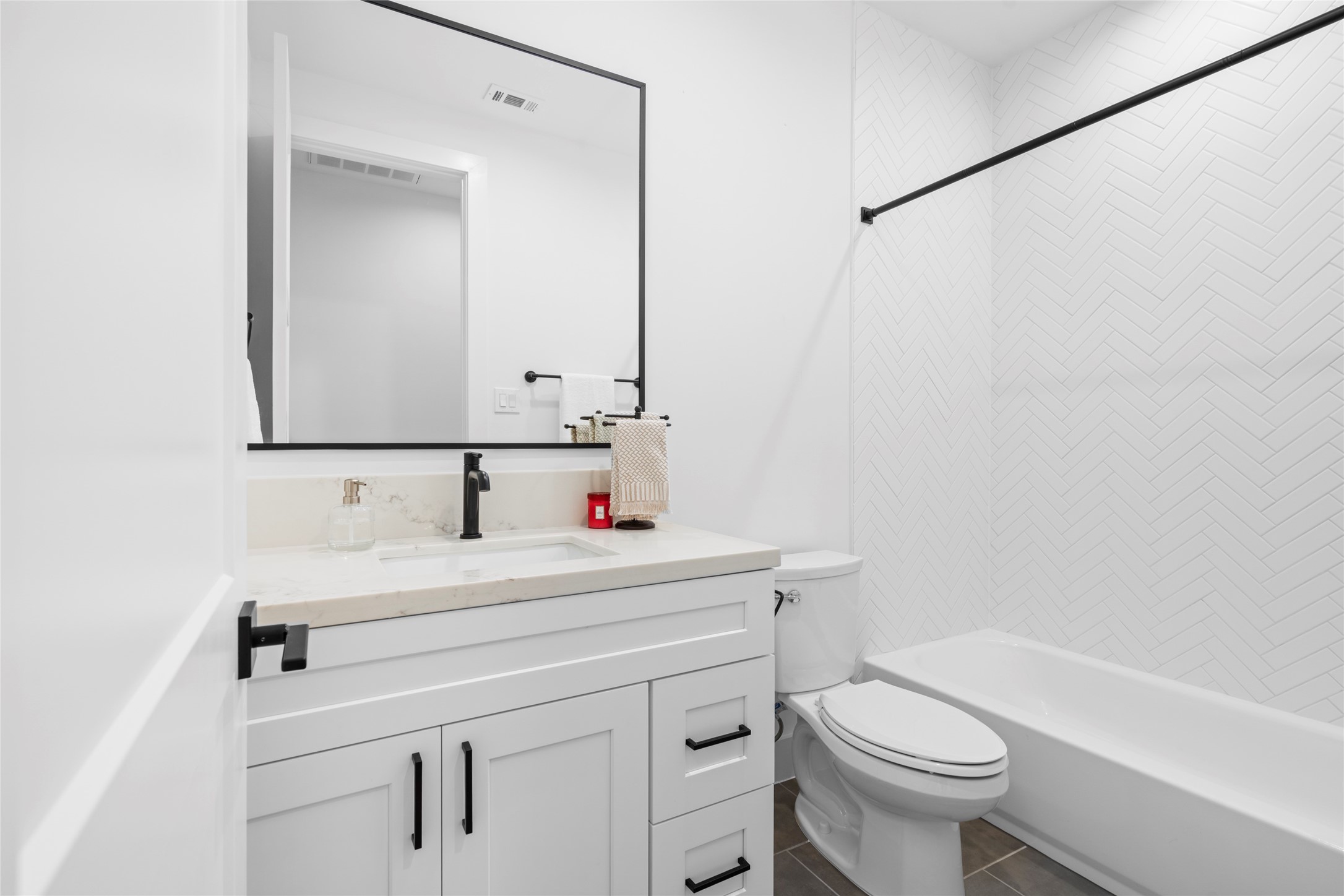 Bathroom shared by bedroom two and three. Quartz counter top, tile, matte black hardware and bathroom fixtures. Metal framed mirror, porcelain floor tile and herringbone ceramic tile in tub/shower.