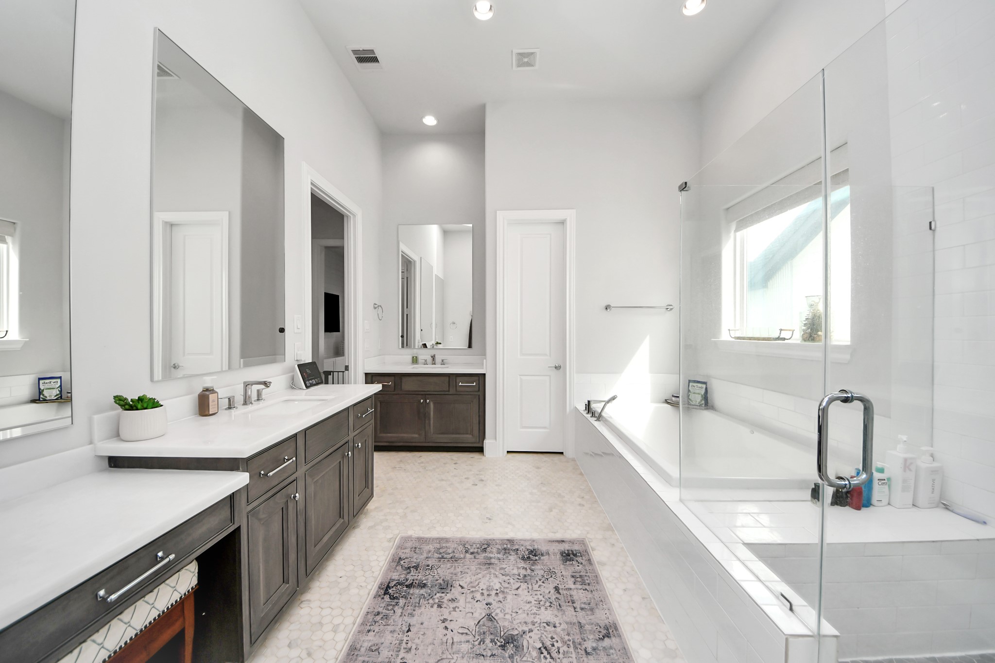 Spacious and elegant bathroom featuring dual vanities with ample storage, a luxurious soaking tub, and a glass-enclosed shower, all set in a chic, light-filled space.