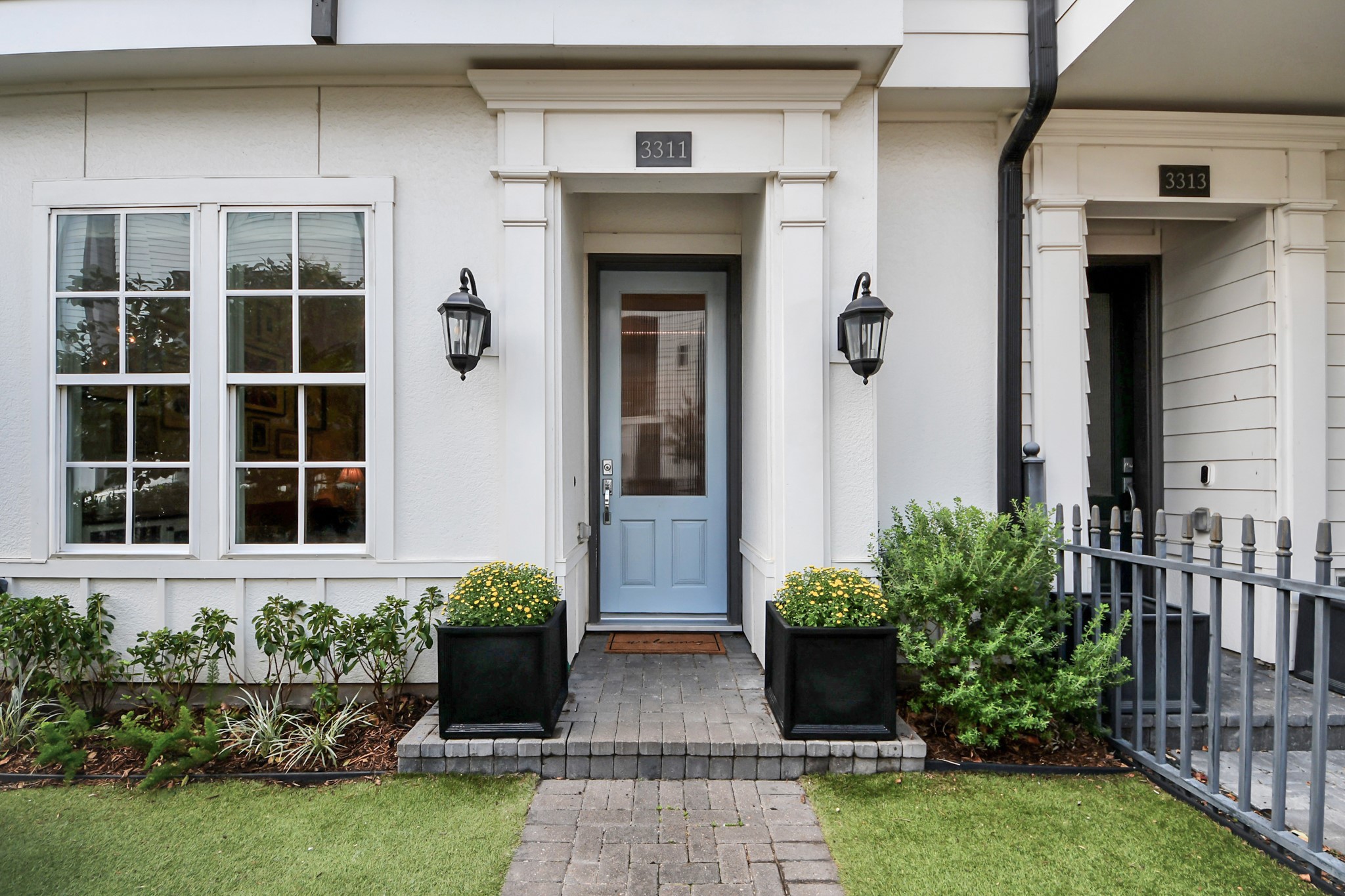 Charming entryway with a welcoming blue door, flanked by elegant lanterns and lush greenery in decorative planters.