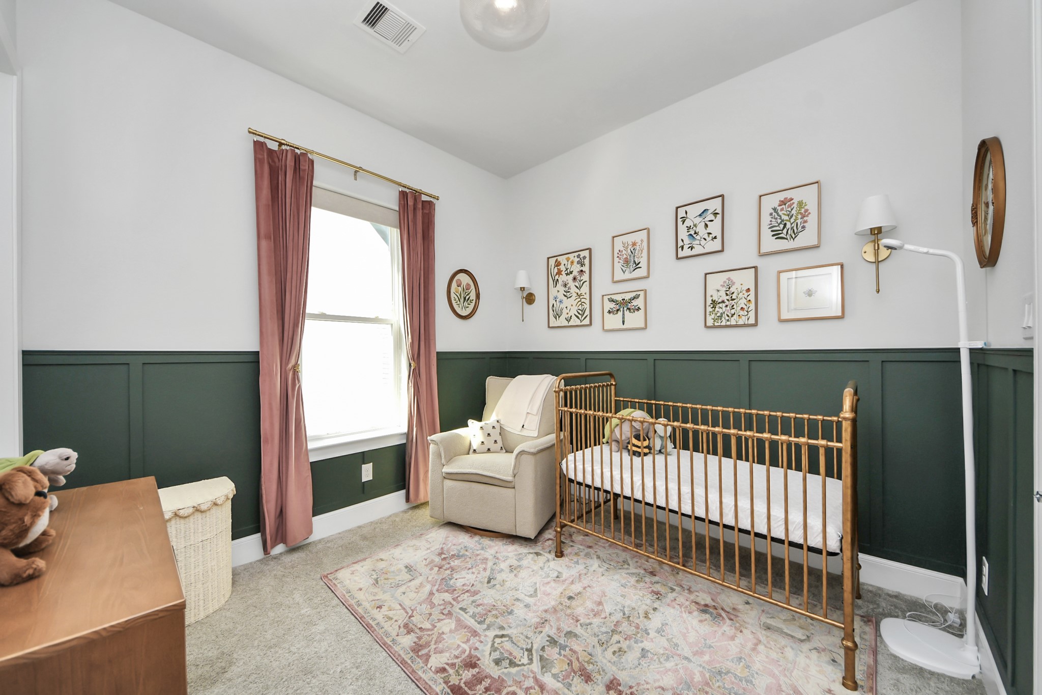 Charming nursery with elegant wainscoting, soft carpeting, and a cozy armchair. The space is adorned with tasteful botanical artwork and features a classic crib, creating a warm and inviting atmosphere.