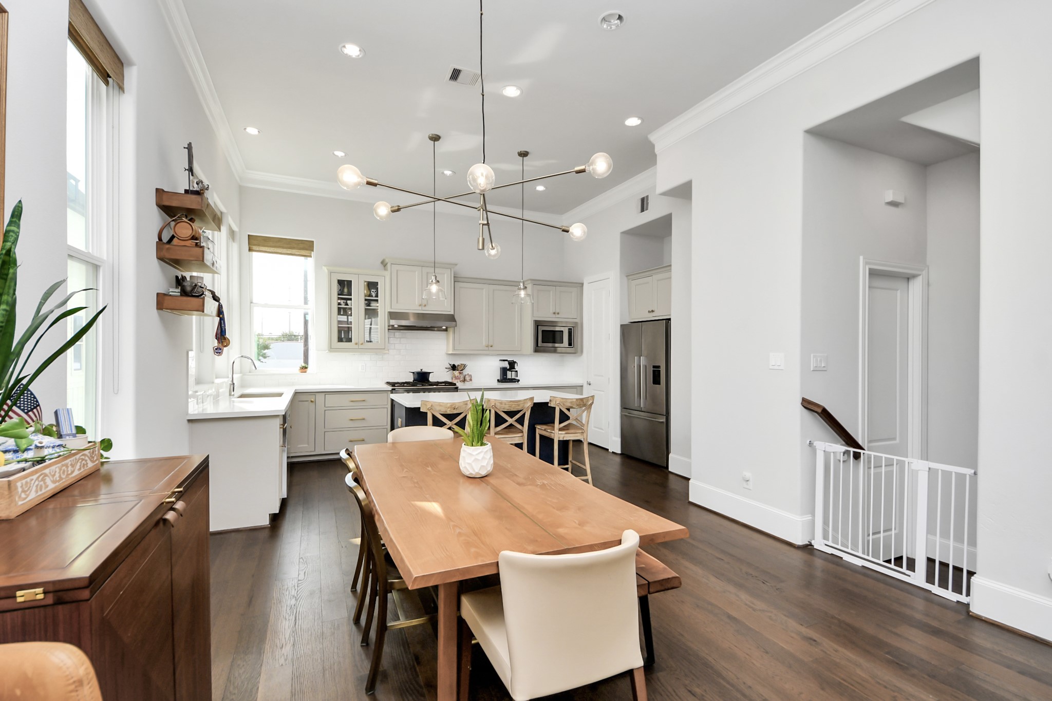 Bright and spacious kitchen and dining area featuring modern light fixtures, sleek cabinetry, and a large wooden dining table, ideal for entertaining.