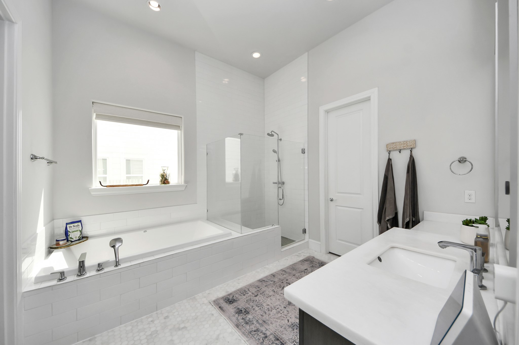 Elegant bathroom featuring a spacious soaking tub, glass-enclosed shower, and modern vanity with sleek fixtures, all bathed in natural light.