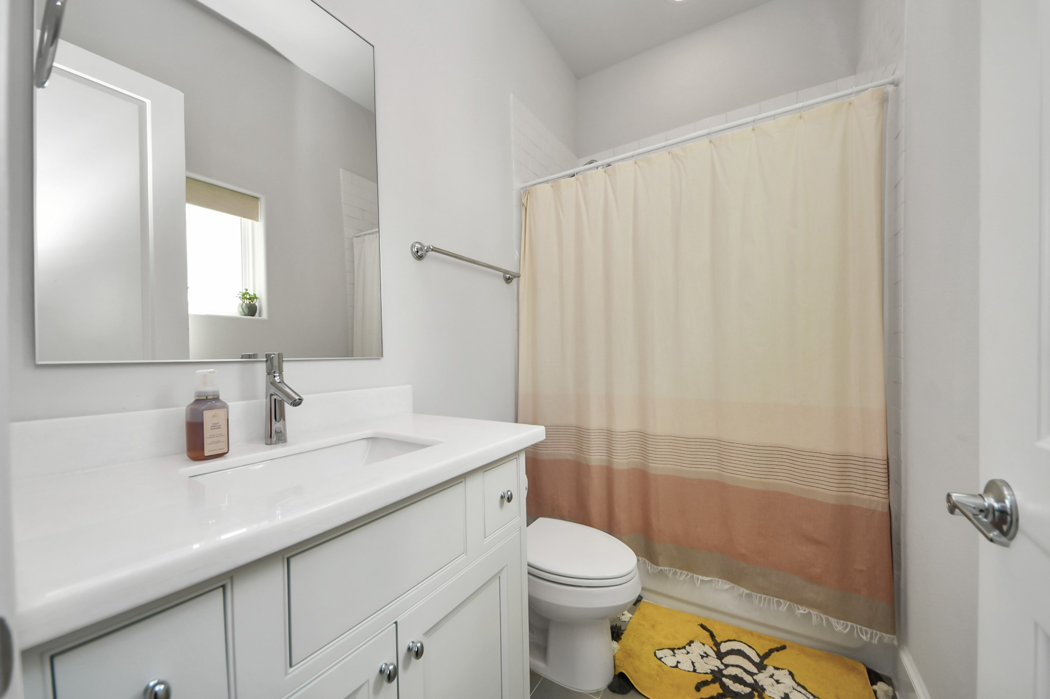 Charming bathroom featuring a sleek white vanity, modern fixtures, and a cozy shower area accented by a neutral-toned curtain.