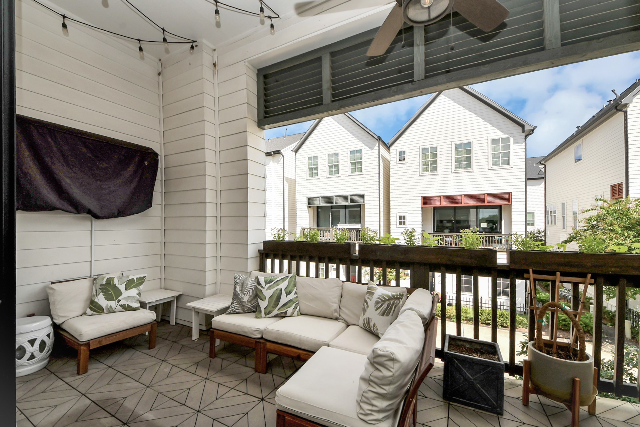 Charming covered patio featuring comfortable seating, stylish tile flooring, and a ceiling fan, perfect for relaxing and enjoying views of the neighboring homes.