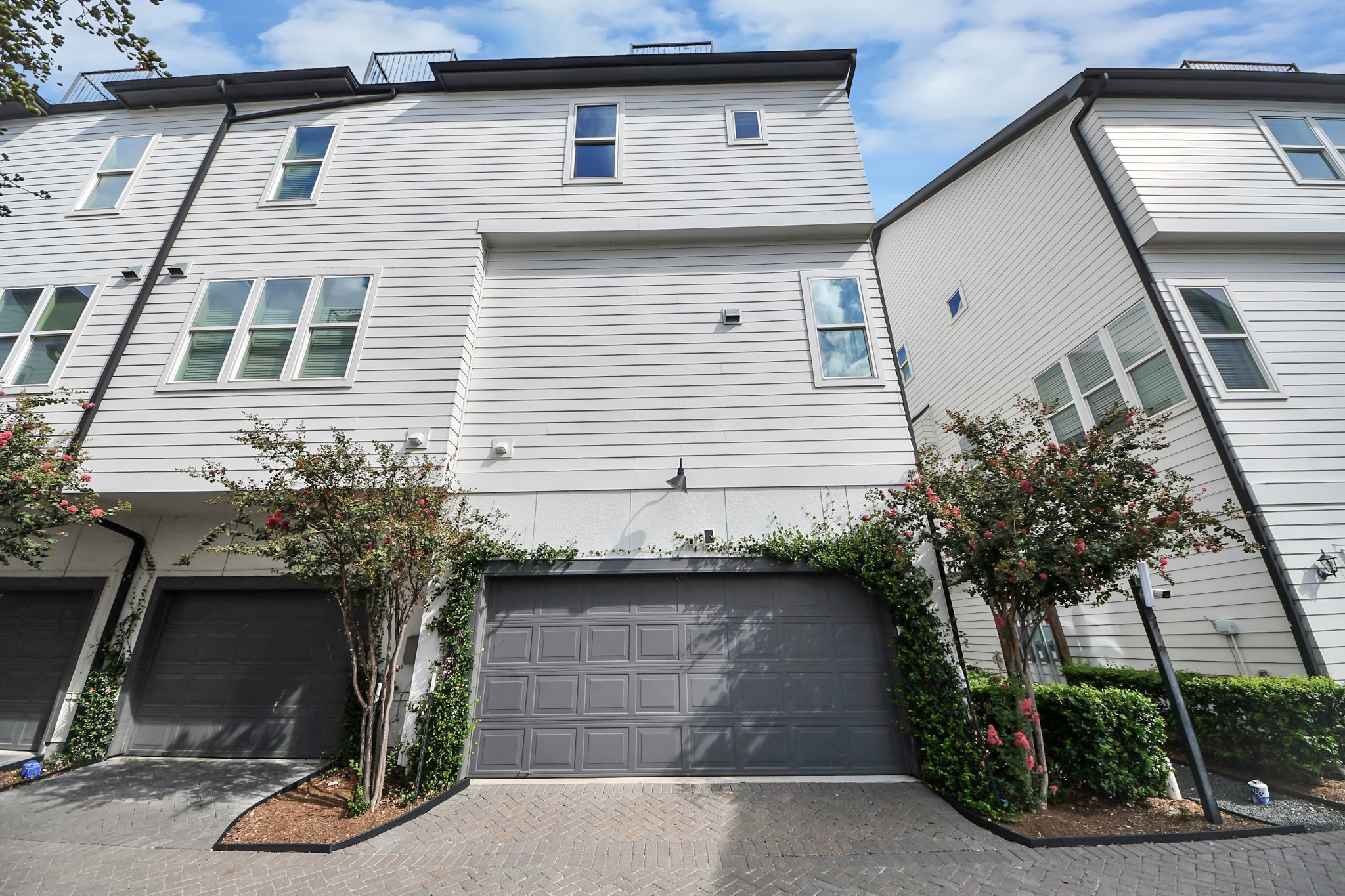 Contemporary townhouse with a sleek facade, featuring a spacious double garage and lush greenery for added curb appeal.