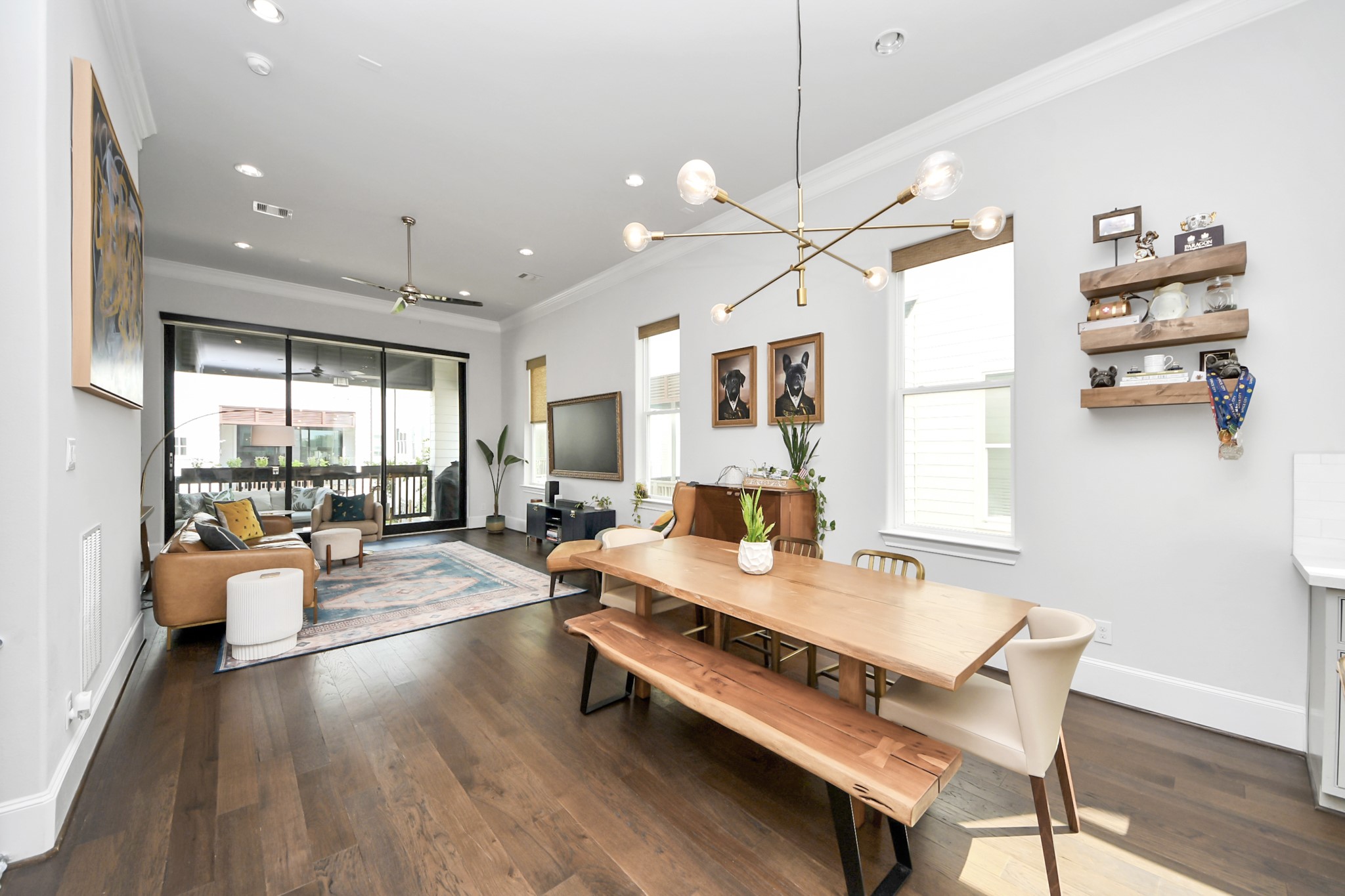 Spacious open-concept living and dining area features elegant hardwood floors, modern lighting, and large windows, leading to a cozy outdoor patio.