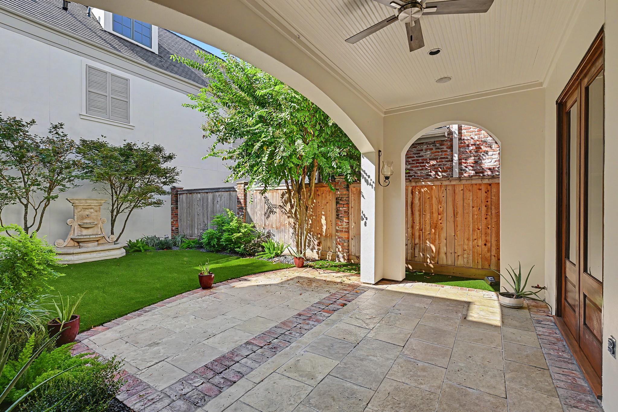 The covered patio provides space for outdoor living, dining, entertaining, or alfresco cooking, with a ceiling fan, direct family room access, and views of the landscaped backyard and fountain.