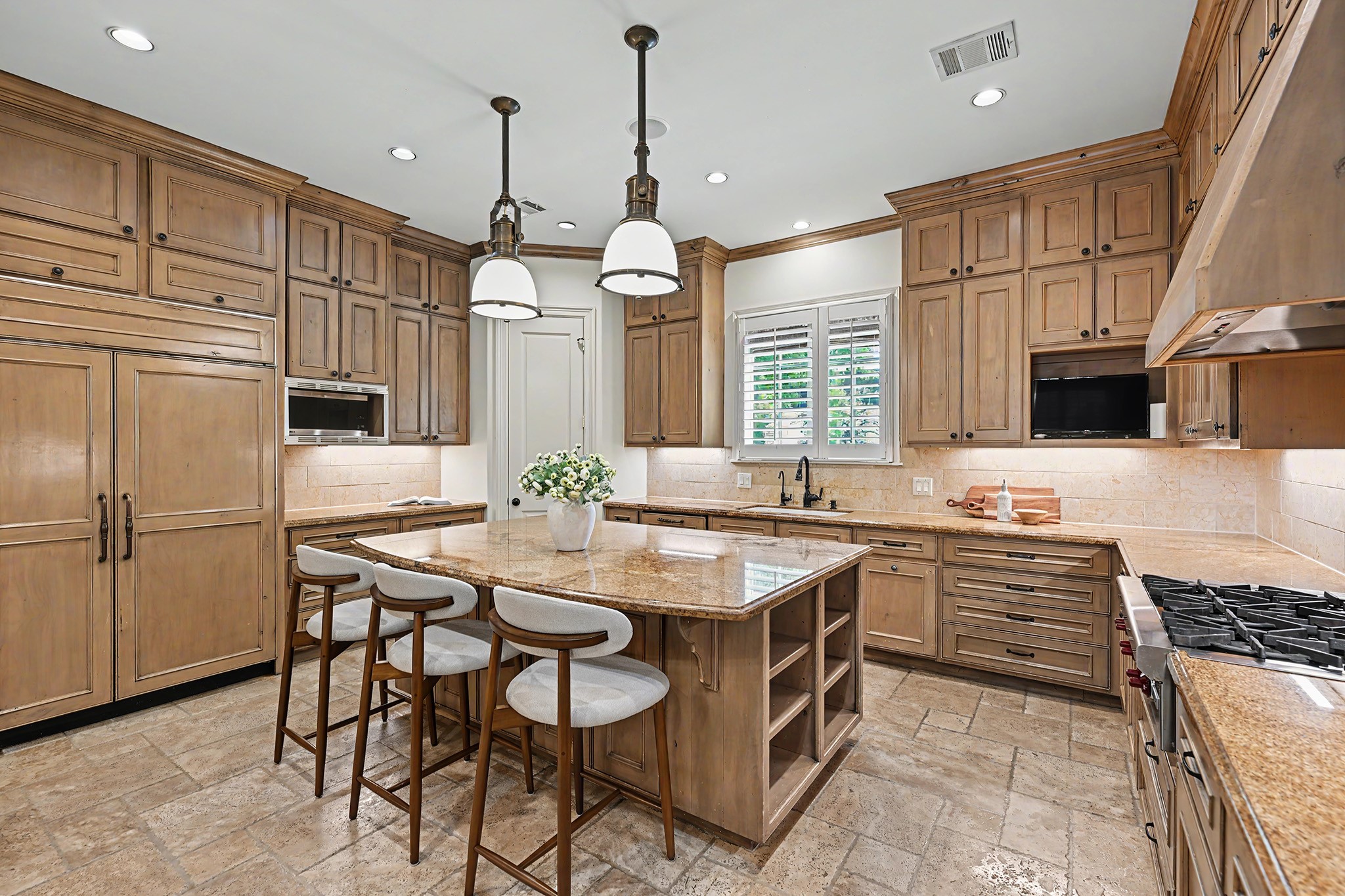 The gourmet kitchen is thoughtfully equipped for everyday cooking and formal entertaining, with ceiling-height cabinetry, pantry, a cabinet-front refrigerator, gas cooktop, and a large center island with bar seating and display shelving.