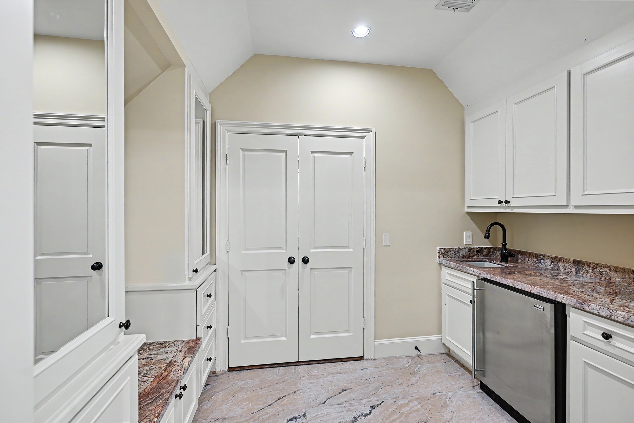 This flex room in the primary suite features a wet bar with beverage refrigerator, cabinetry, and drawers, along with a dedicated dressing area with mirrored cabinets and a built-in shoe bench.