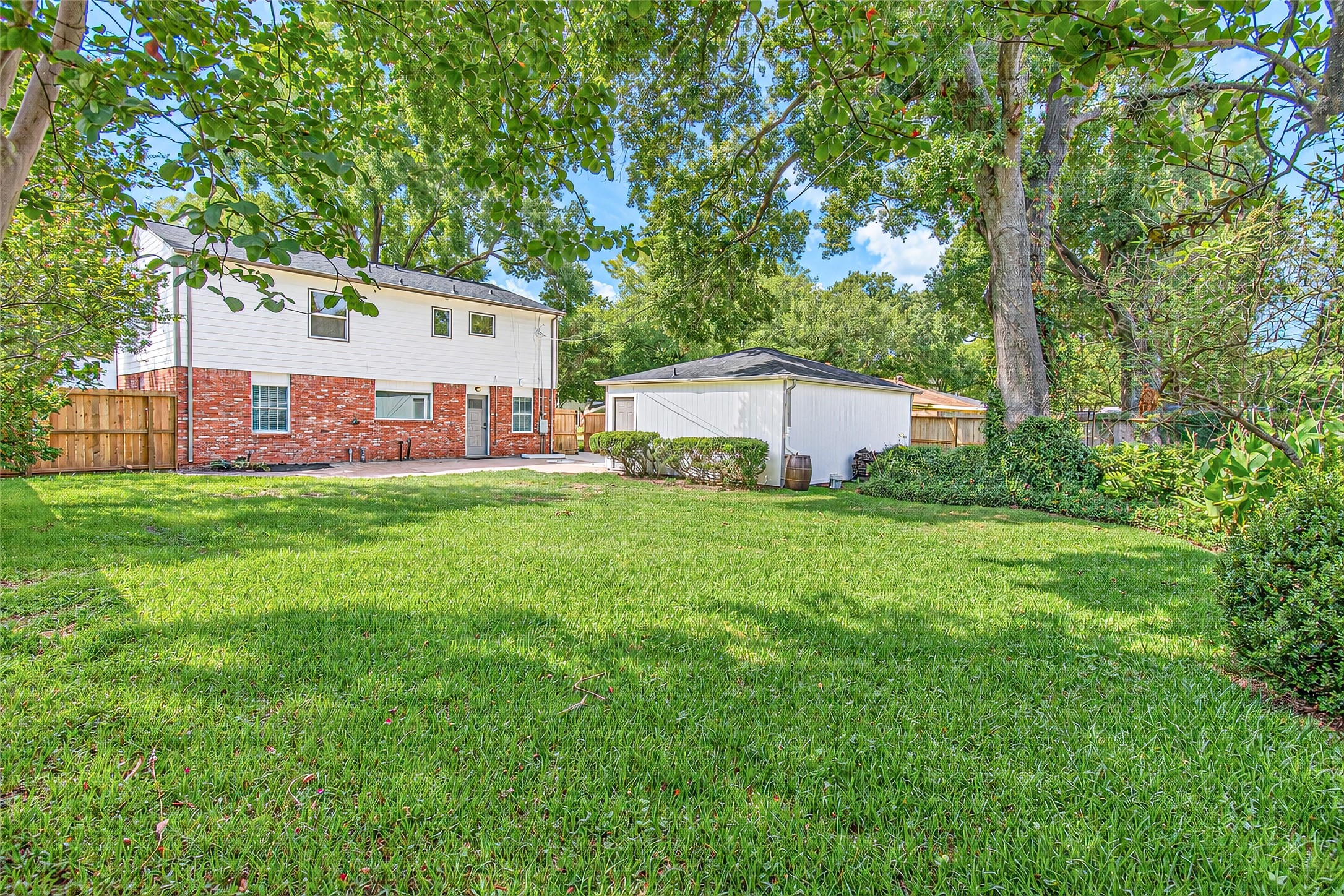 Spacious backyard with lush green lawn, charming brick and siding exterior, and a detached garage, all surrounded by mature trees for added privacy.