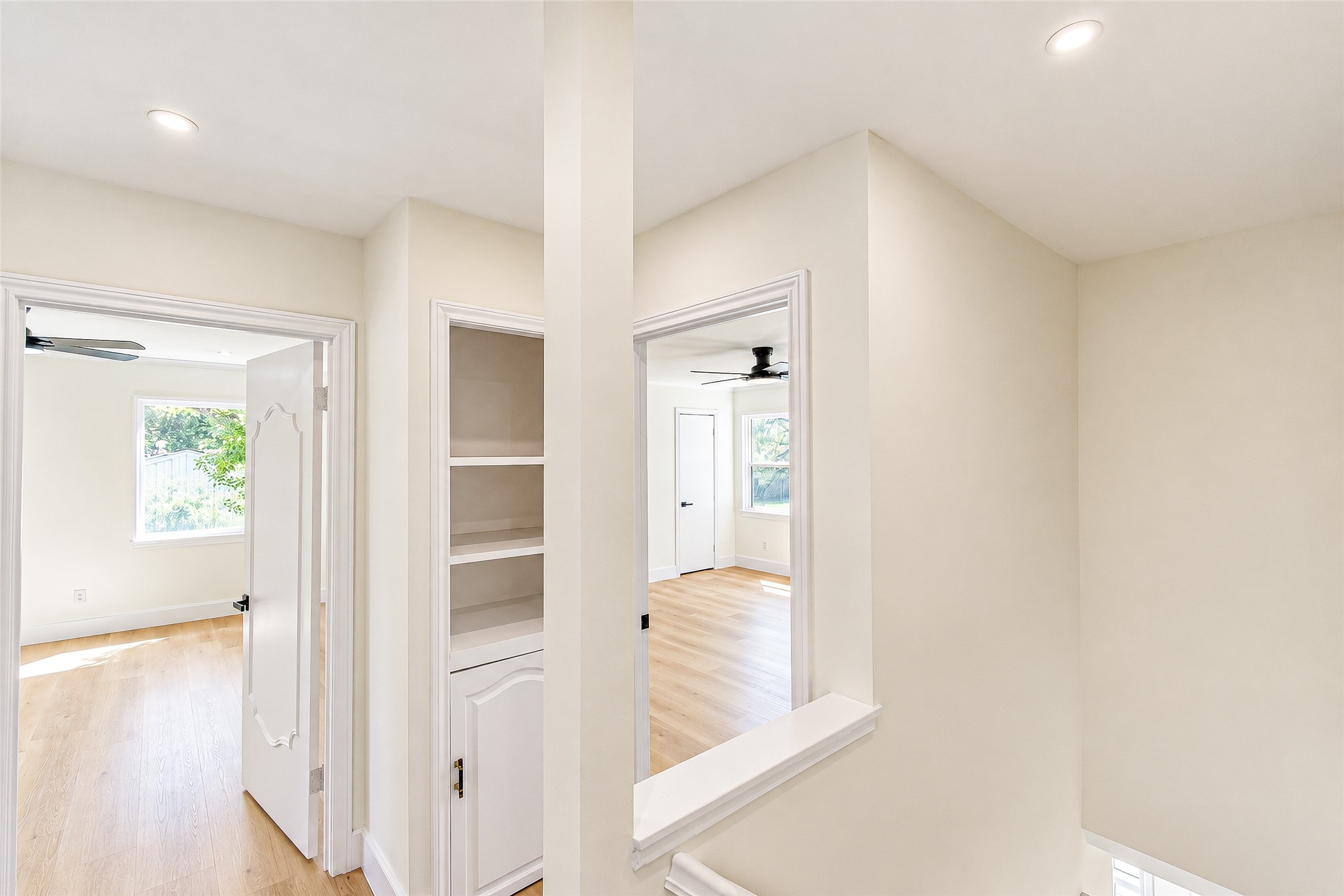 Bright and airy hallway with built-in shelving and access to spacious rooms featuring large windows and sleek ceiling fans.