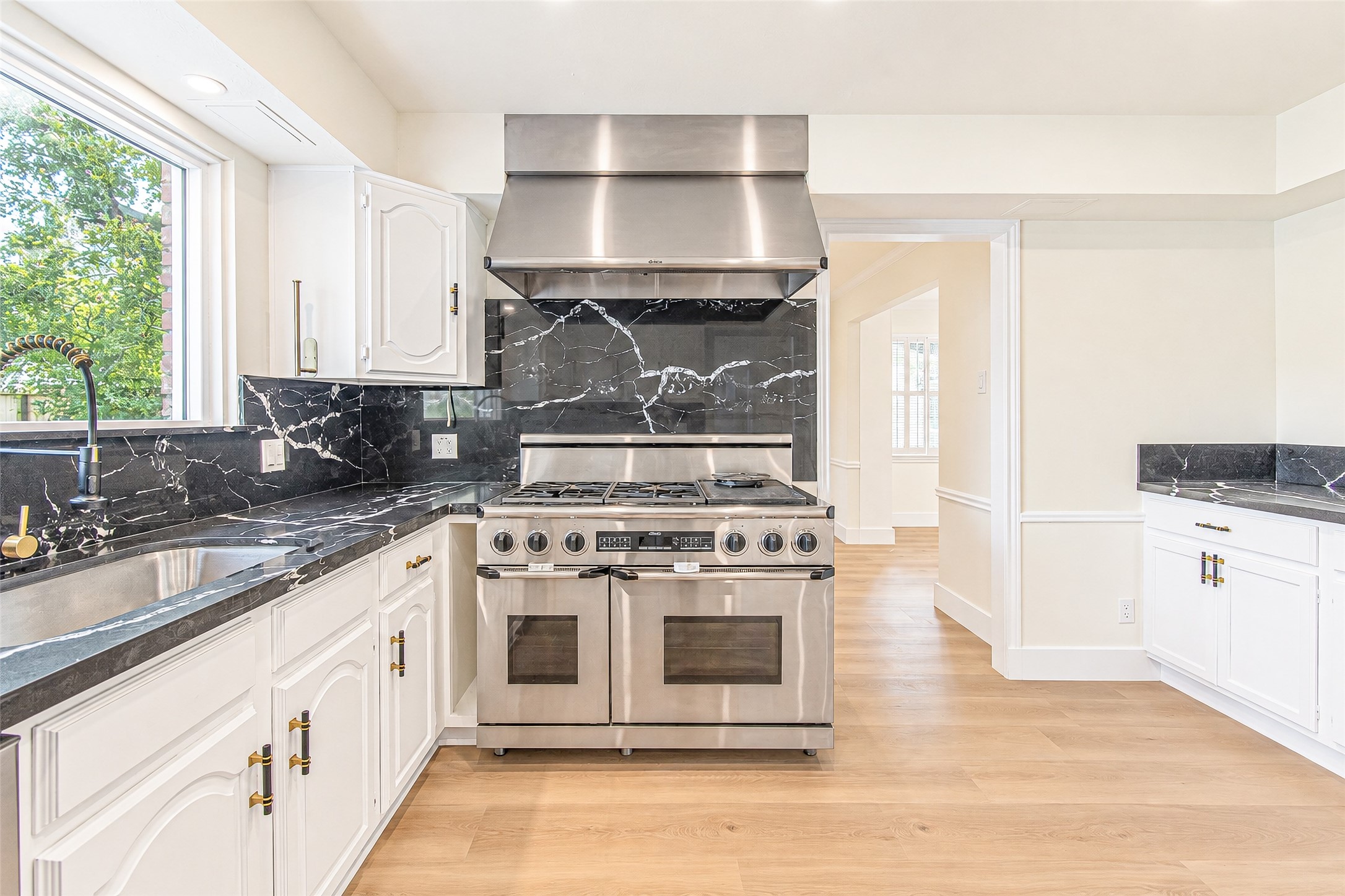 Modern kitchen featuring a sleek stainless steel stove, elegant black quartz countertops, and white cabinetry with stylish brass handles.