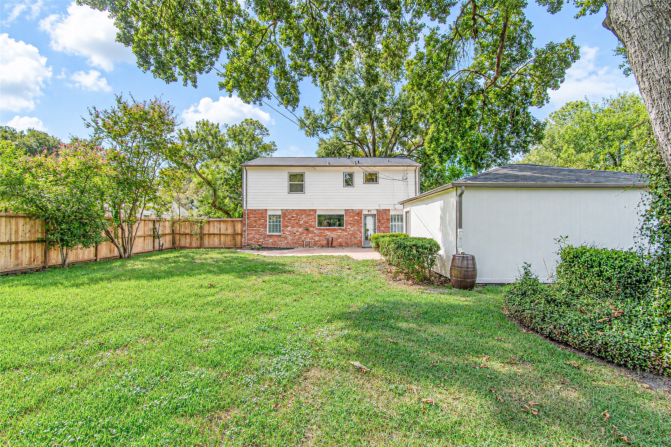 Spacious backyard with lush green grass, mature trees, and a privacy fence, complemented by a charming two-story home featuring a mix of brick and siding.