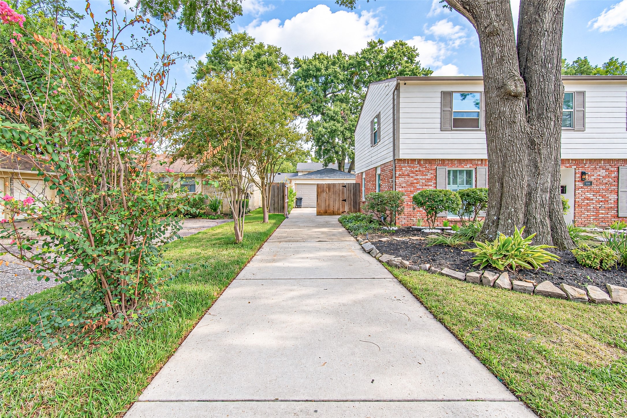 Charming two-story home with classic brick exterior, framed by mature trees and lush landscaping, leading to a welcoming front walkway.