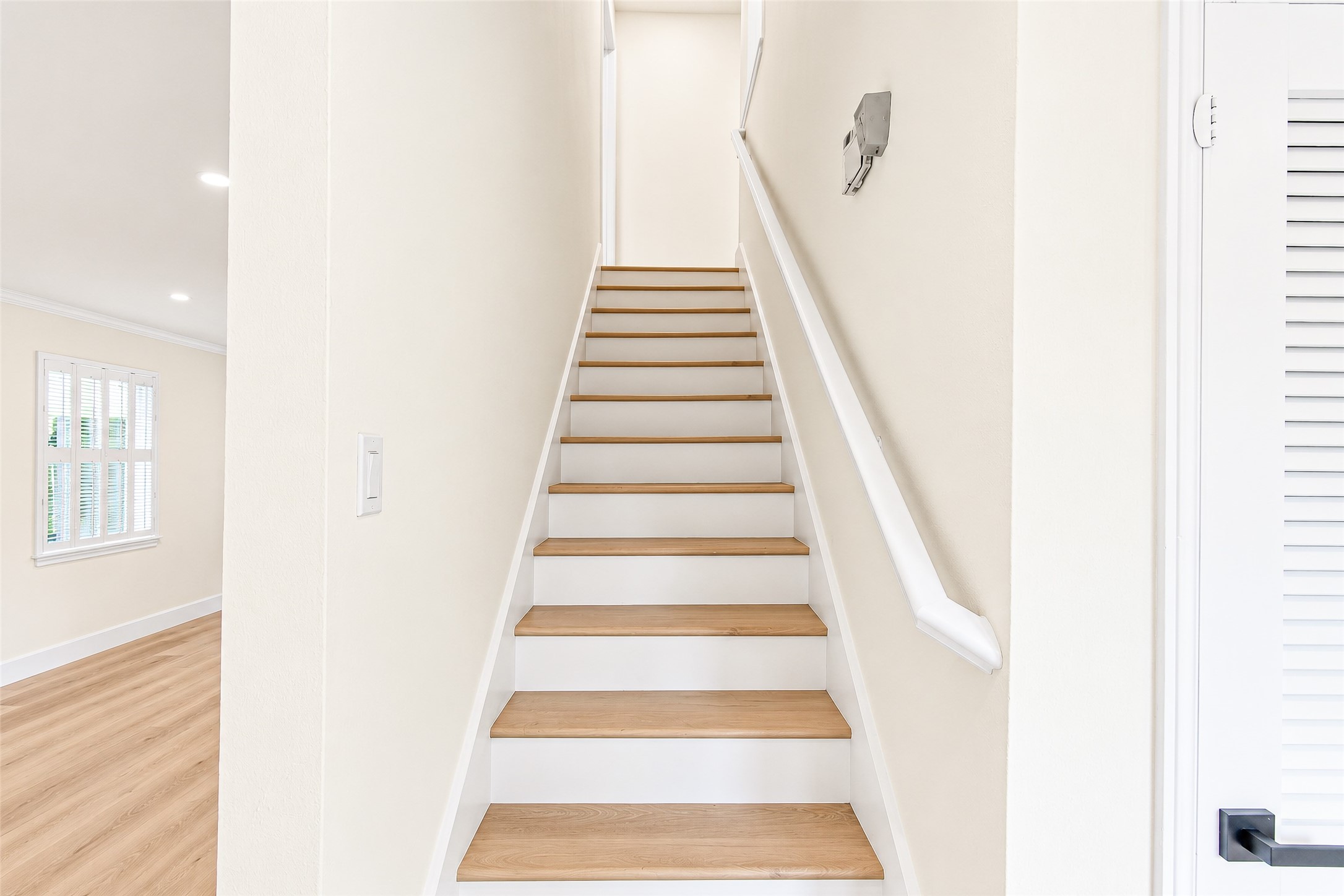 Bright and inviting staircase with natural vinyl steps leads to the upper level, complemented by fresh white walls and a sleek handrail.