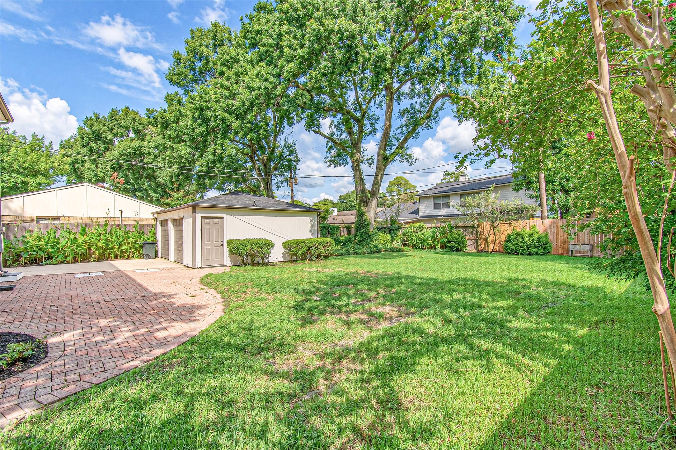 Spacious backyard with lush green lawn, mature trees, and a charming brick patio, perfect for outdoor gatherings.