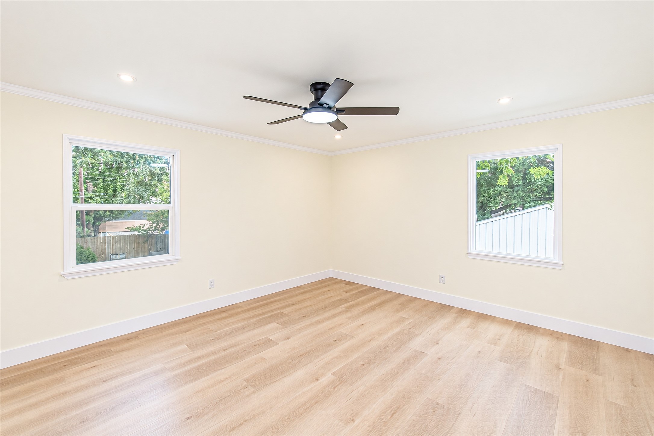 Experience tranquility in this spacious primary bedroom, featuring abundant natural light, elegant vinyl flooring, and a modern ceiling fan for ultimate comfort.