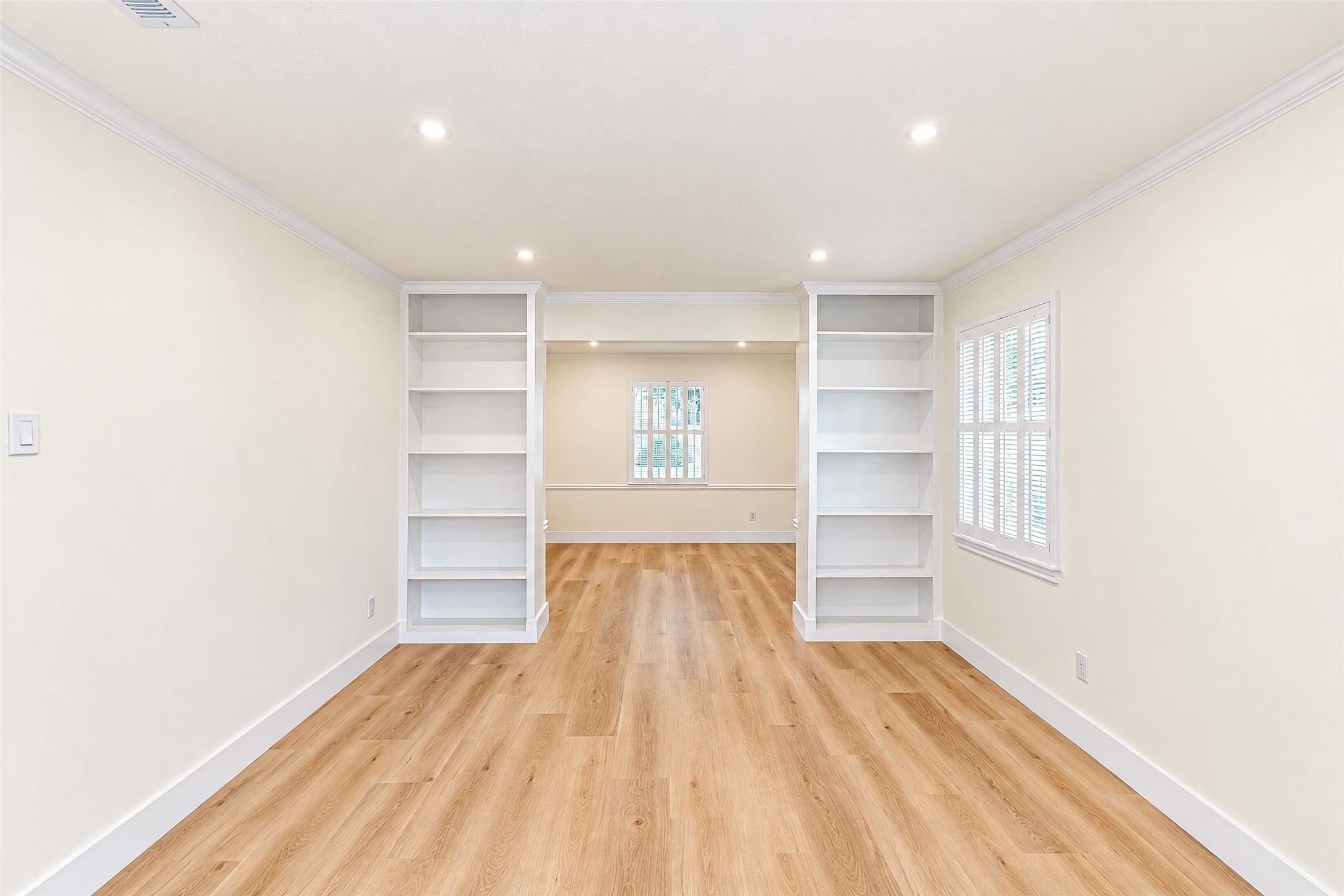 Bright and inviting study featuring elegant built-in bookshelves, warm floors, and ample natural light for a perfect work-from-home retreat.