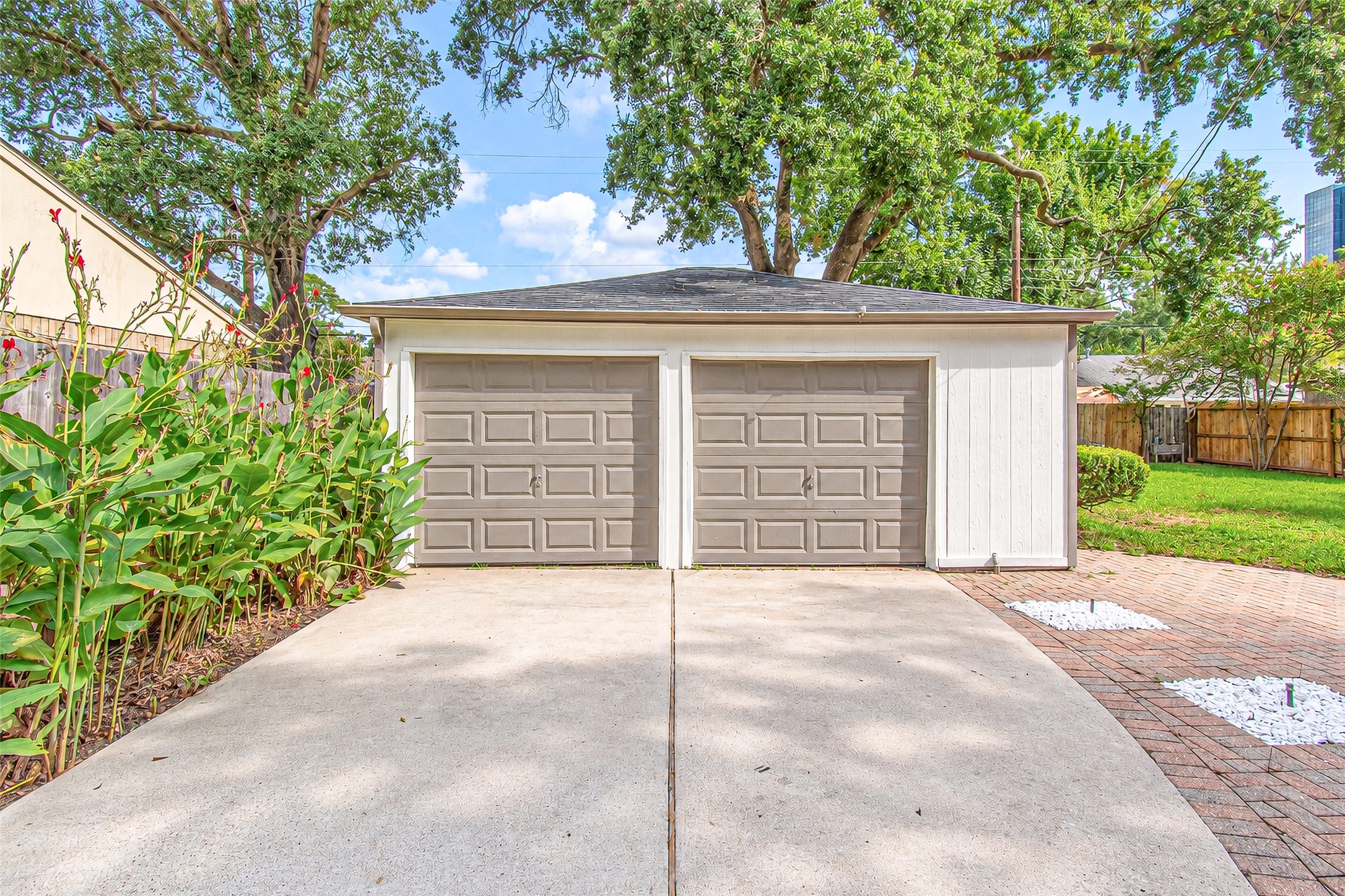 Spacious double garage with a wide driveway, surrounded by lush greenery and mature trees, offering ample storage and parking space.