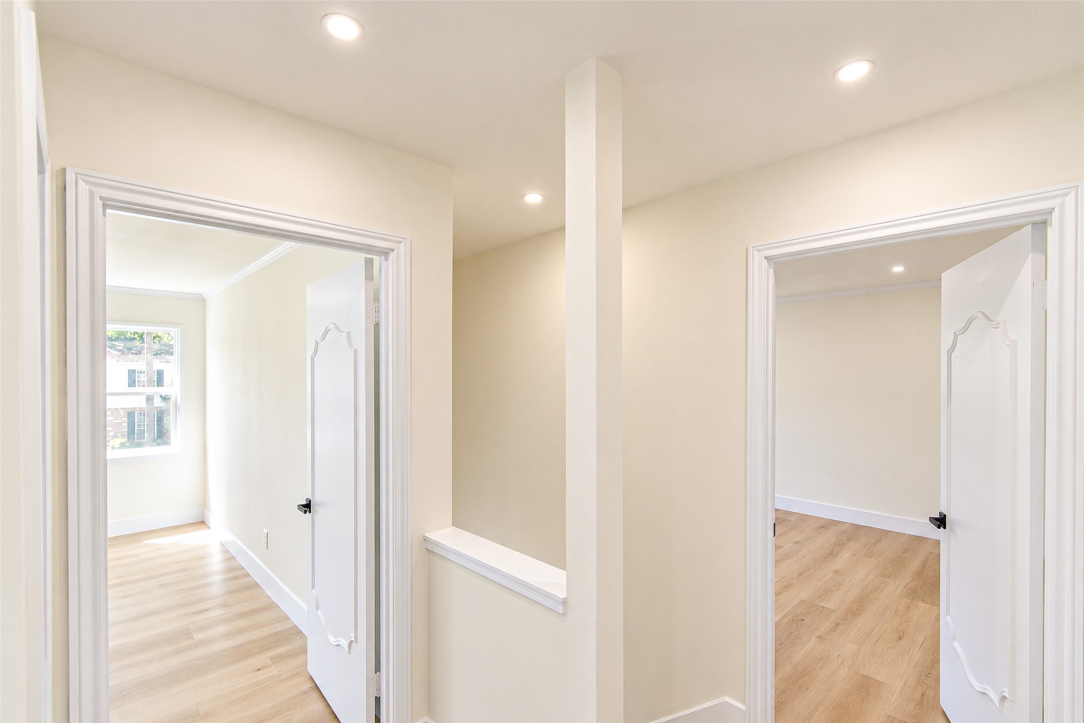 Bright and inviting hallway with elegant white doors leading to sunlit rooms, featuring light wood flooring and recessed lighting.