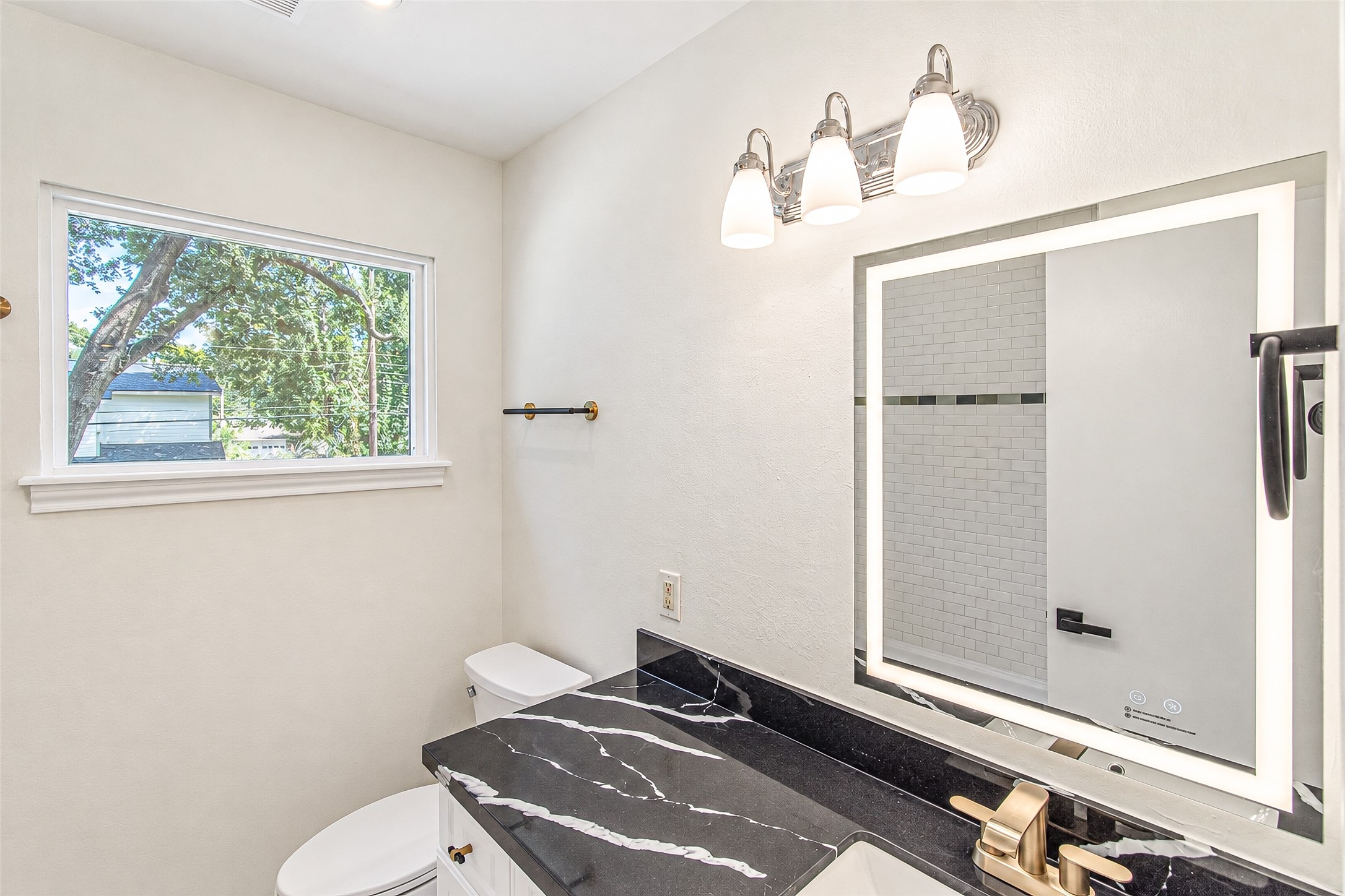 The second bath boasts a sleek design with a modern black countertop, elegant gold fixtures, and a bright window, creating a refreshing and stylish space.