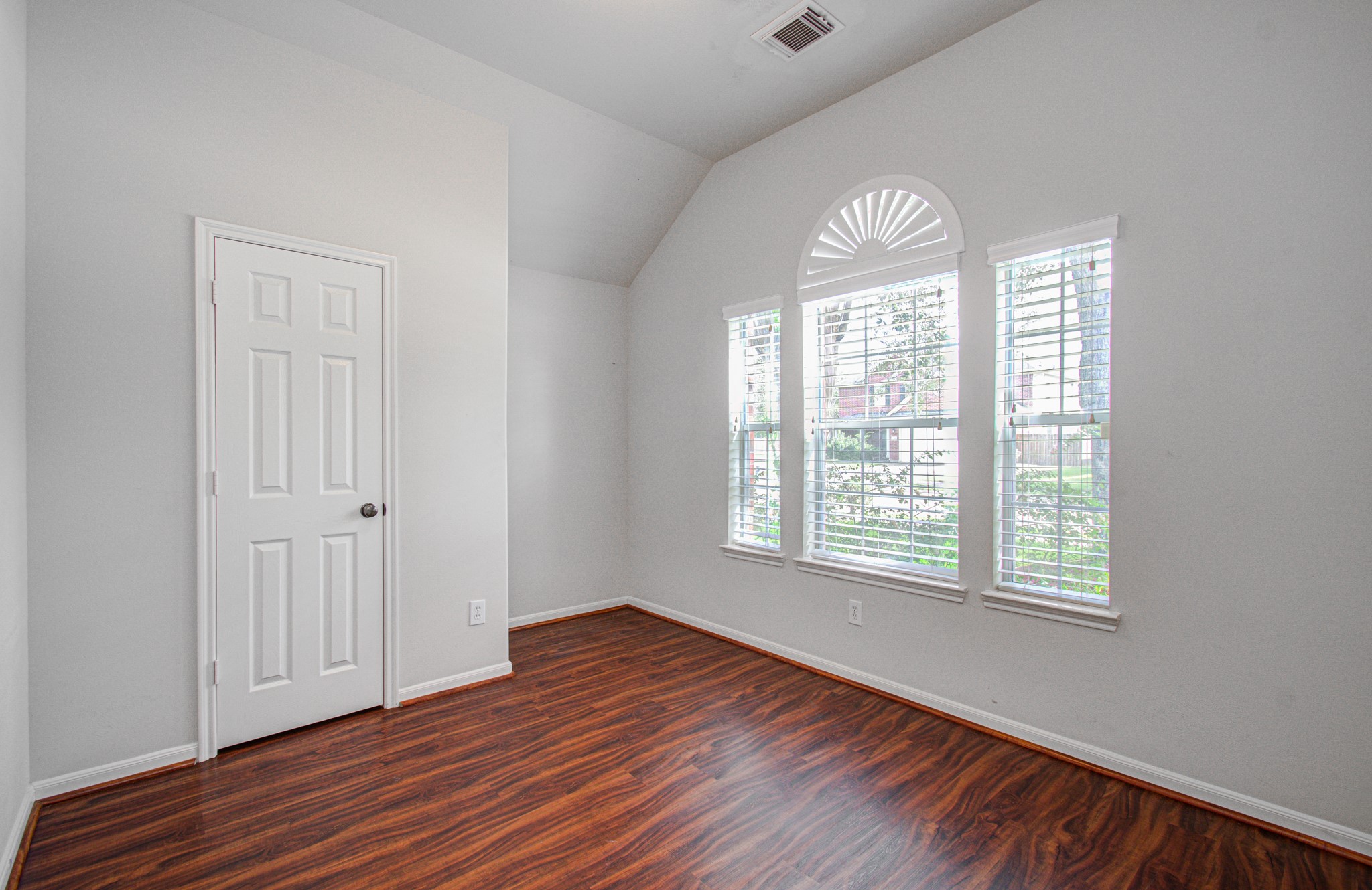 Bright bedroom featuring elegant arched windows and rich wood flooring, and a vaulted ceiling for a cozy and inviting space.
