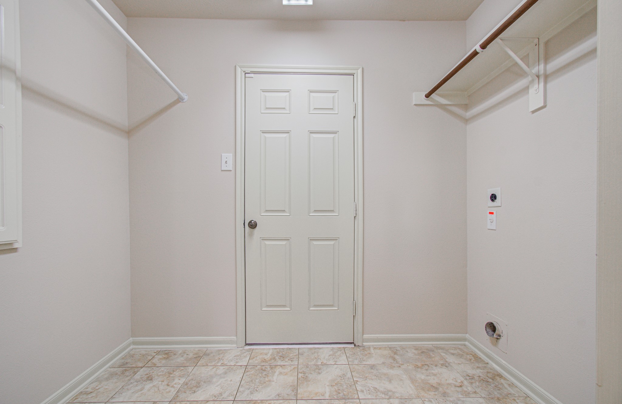 Spacious laundry room with tiled flooring, ample shelving, and space for washer and dryer installation.