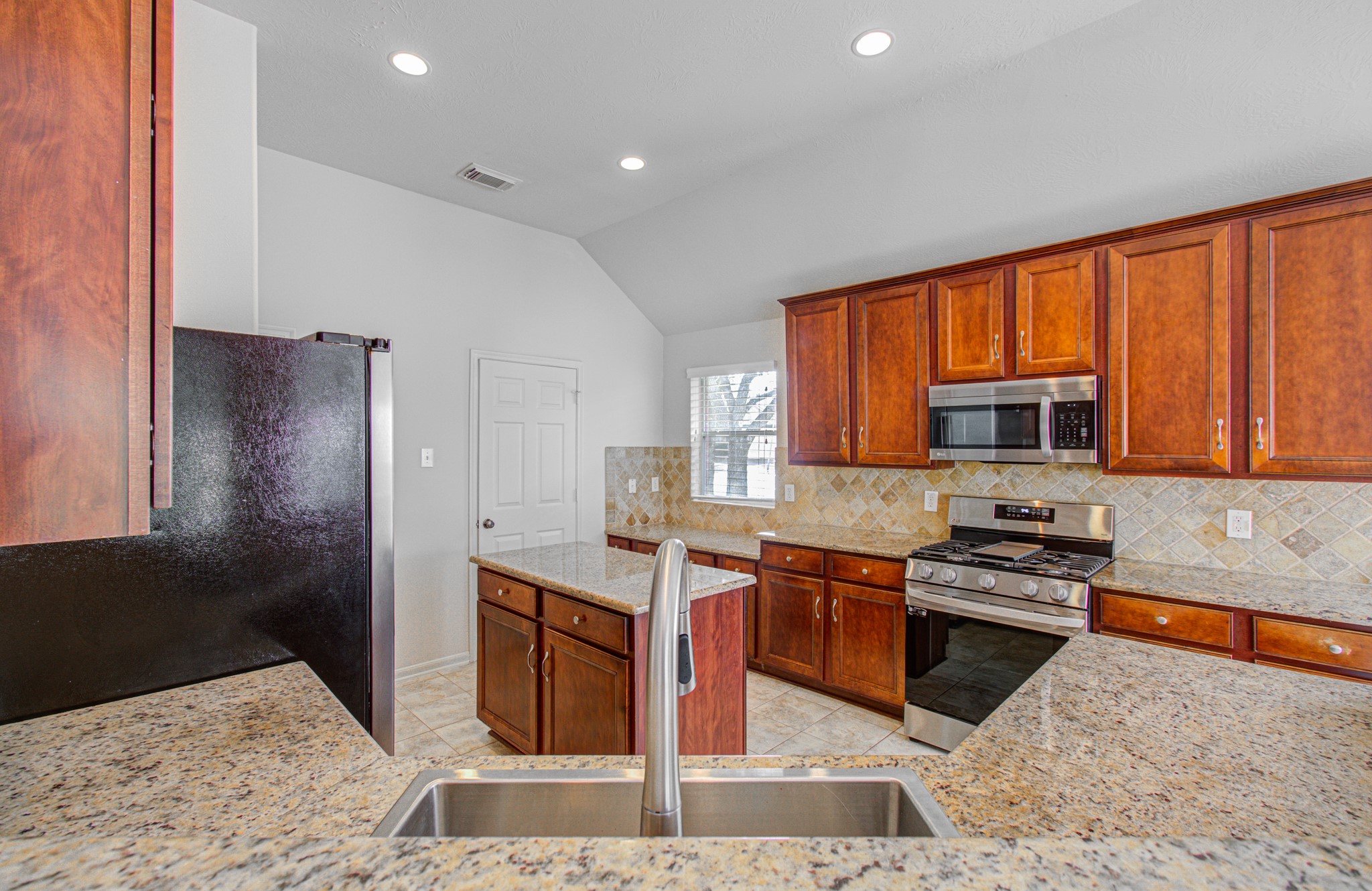 Elegant kitchen featuring rich wood cabinetry, granite countertops, and modern stainless steel appliances, complemented by a stylish tile backsplash.