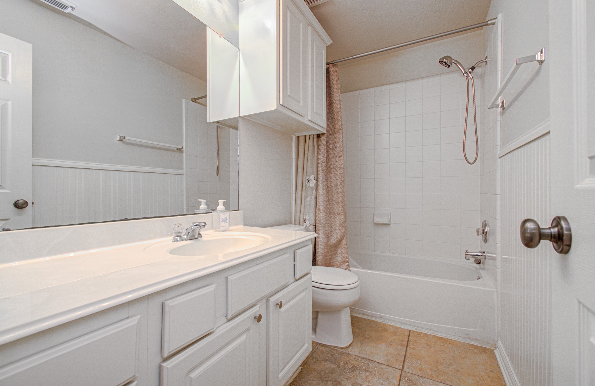 Bright and clean bathroom featuring a spacious vanity with ample storage, a tub-shower combination with elegant fixtures, and neutral tile flooring.