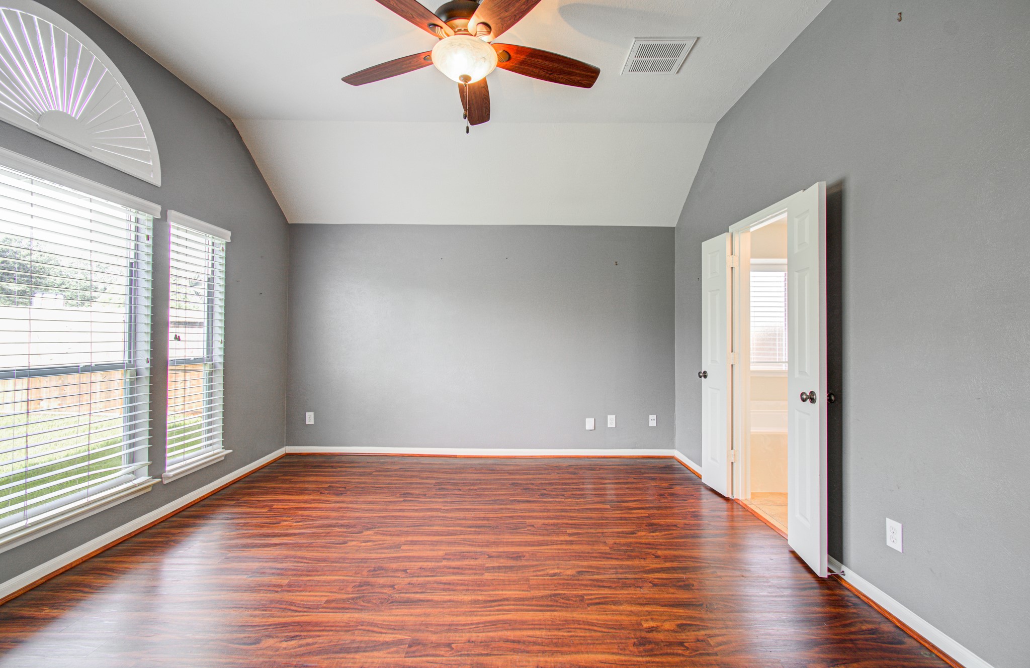 Primary bedroom with vaulted ceilings, rich wood flooring, and abundant natural light from large windows.