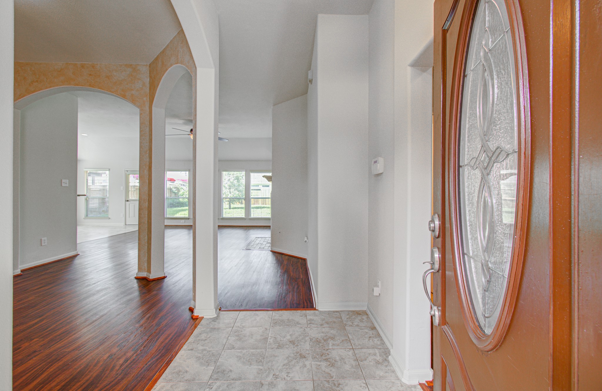 Inviting entryway with elegant tile flooring and a warm wooden door, leading into an open living area featuring rich wood floors and ample natural light.
