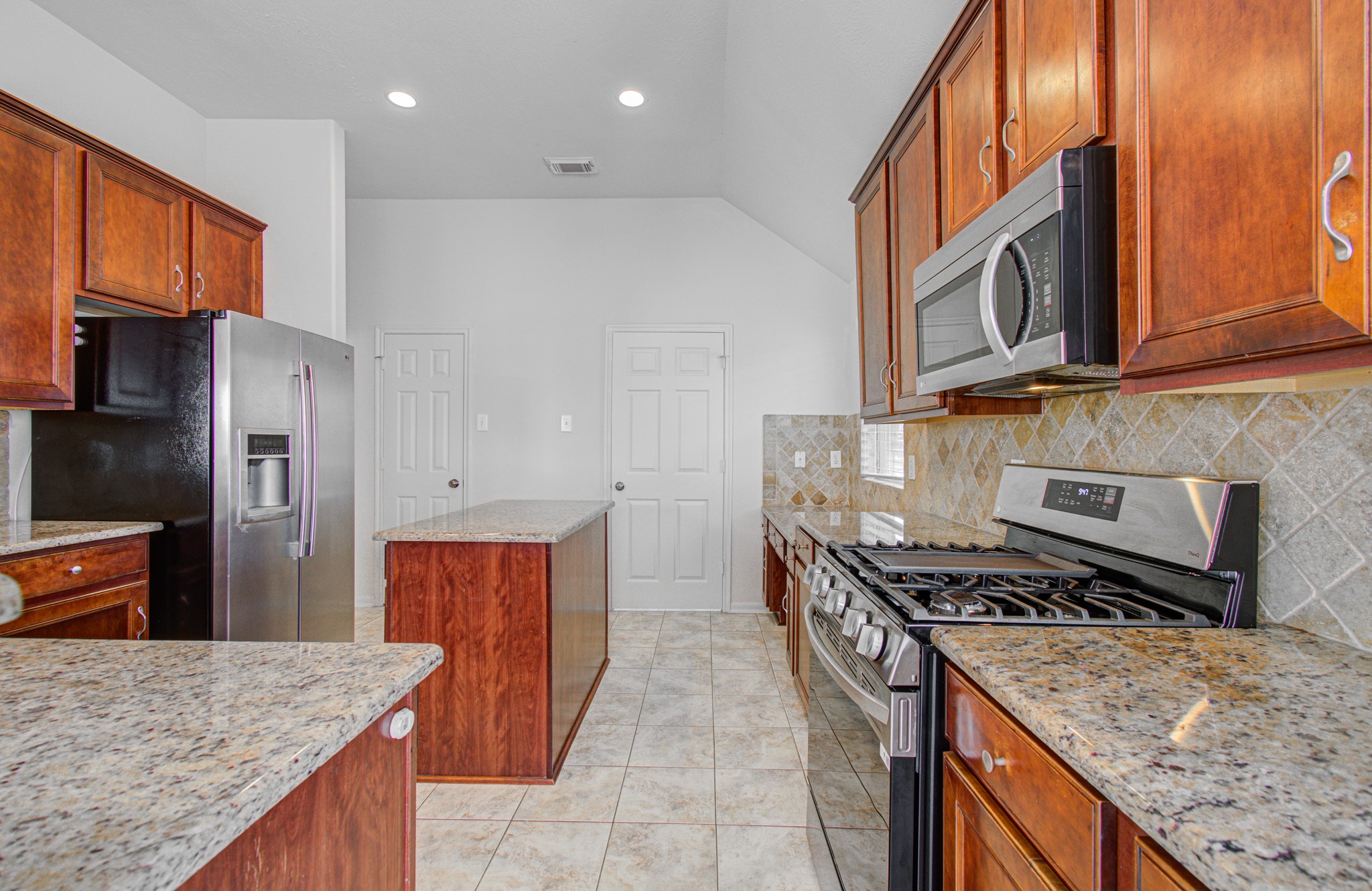 Spacious kitchen with elegant granite countertops, rich wooden cabinetry, and modern stainless steel appliances, including a gas stove and side-by-side refrigerator.