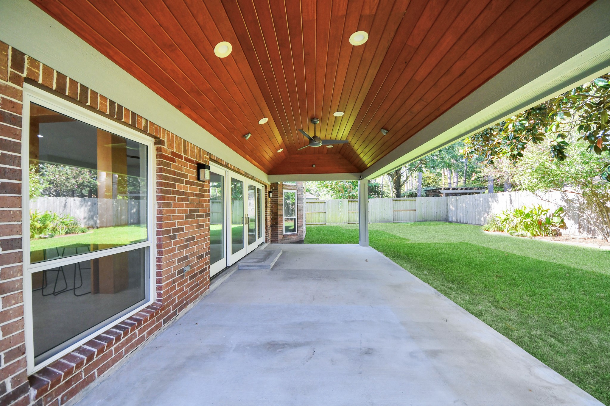 Left view of the spacious covered back patio with a luxurious wood ceiling and lights with a fan