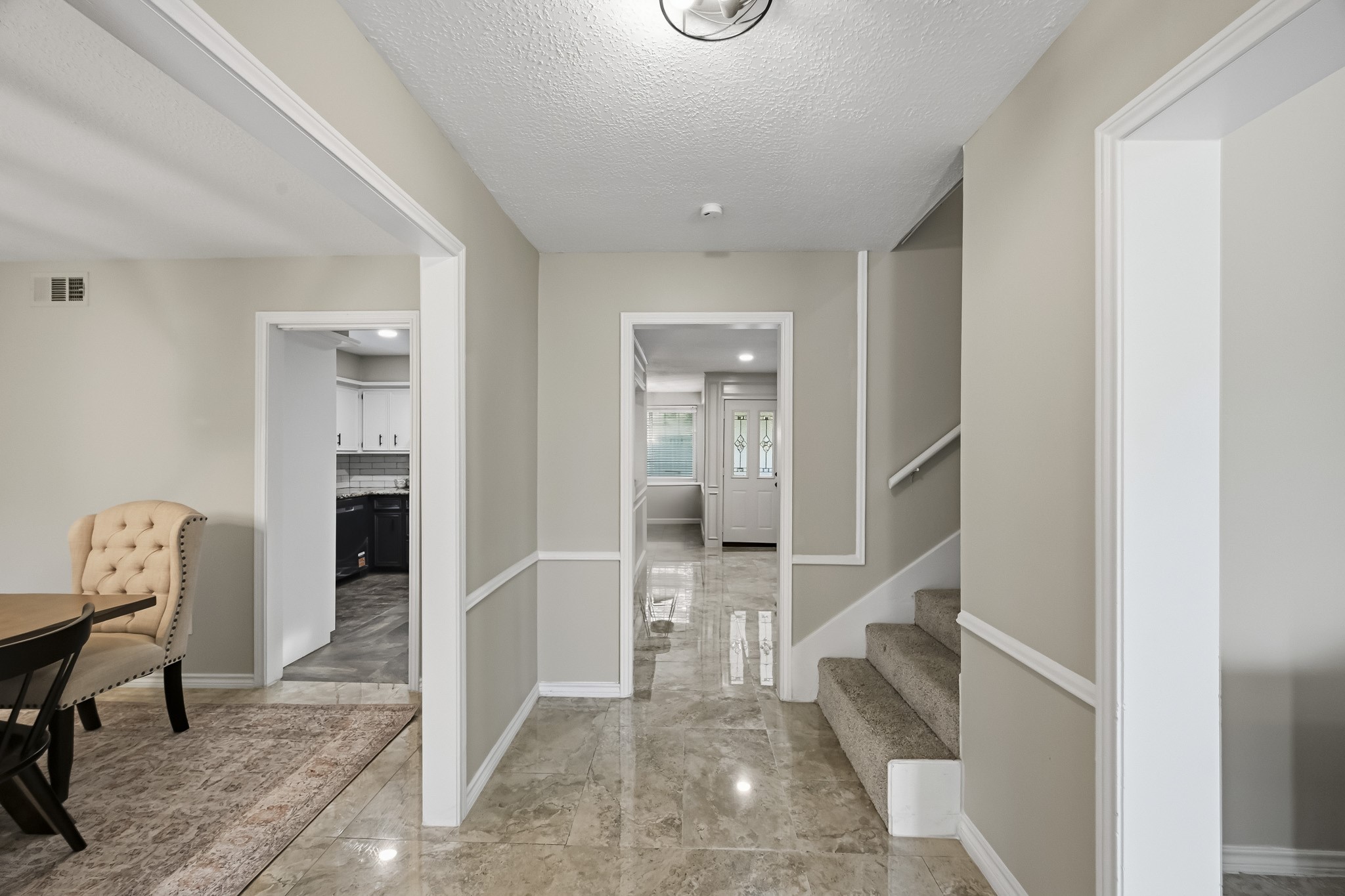 Elegant entryway with gleaming tile floors, leading to a bright living area and cozy carpeted staircase. Adjacent dining room and modern kitchen offer seamless flow for entertaining.