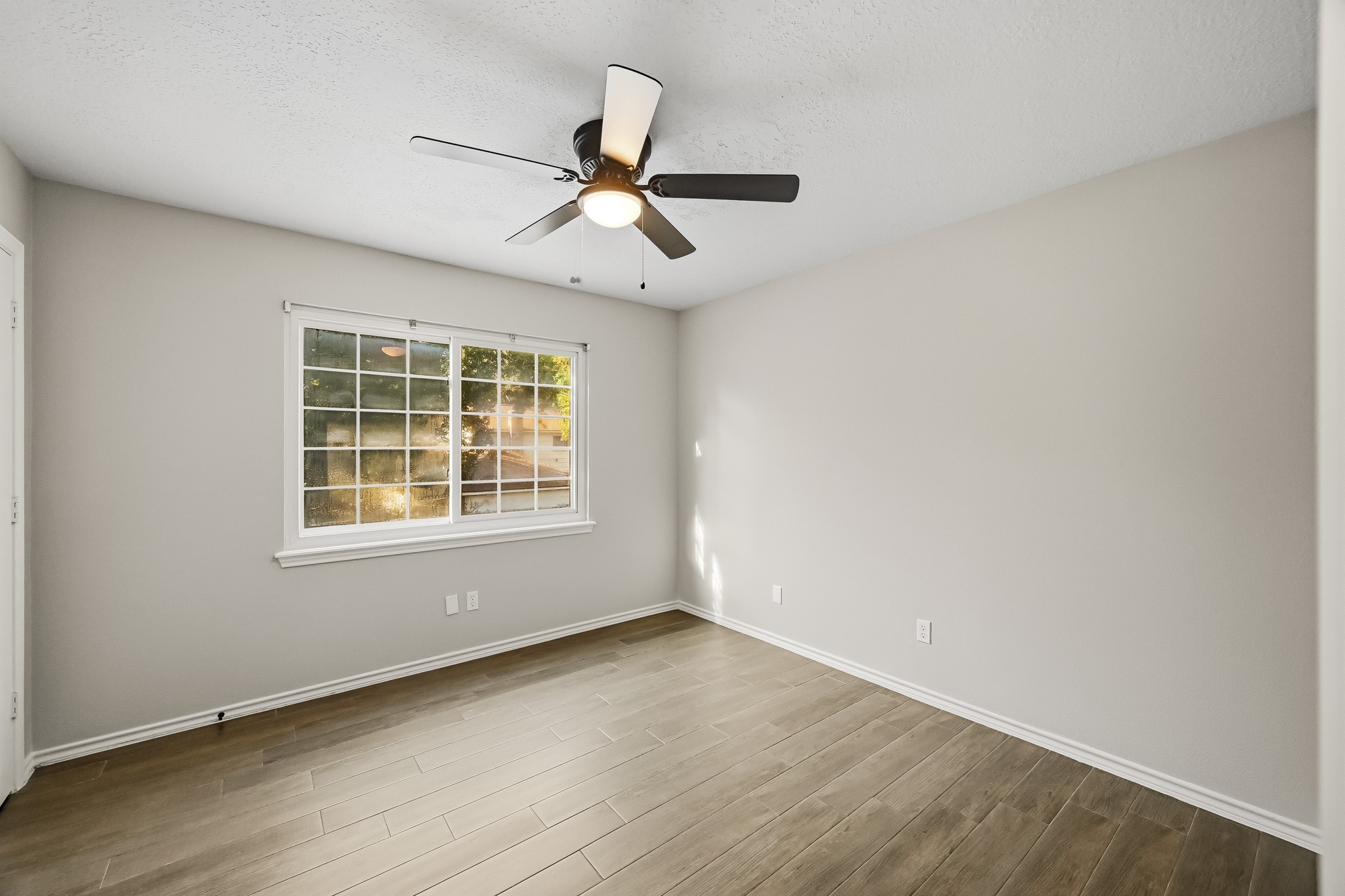 Bright and inviting room with sleek wood-look flooring, a modern ceiling fan, and a large window that fills the space with natural light.
