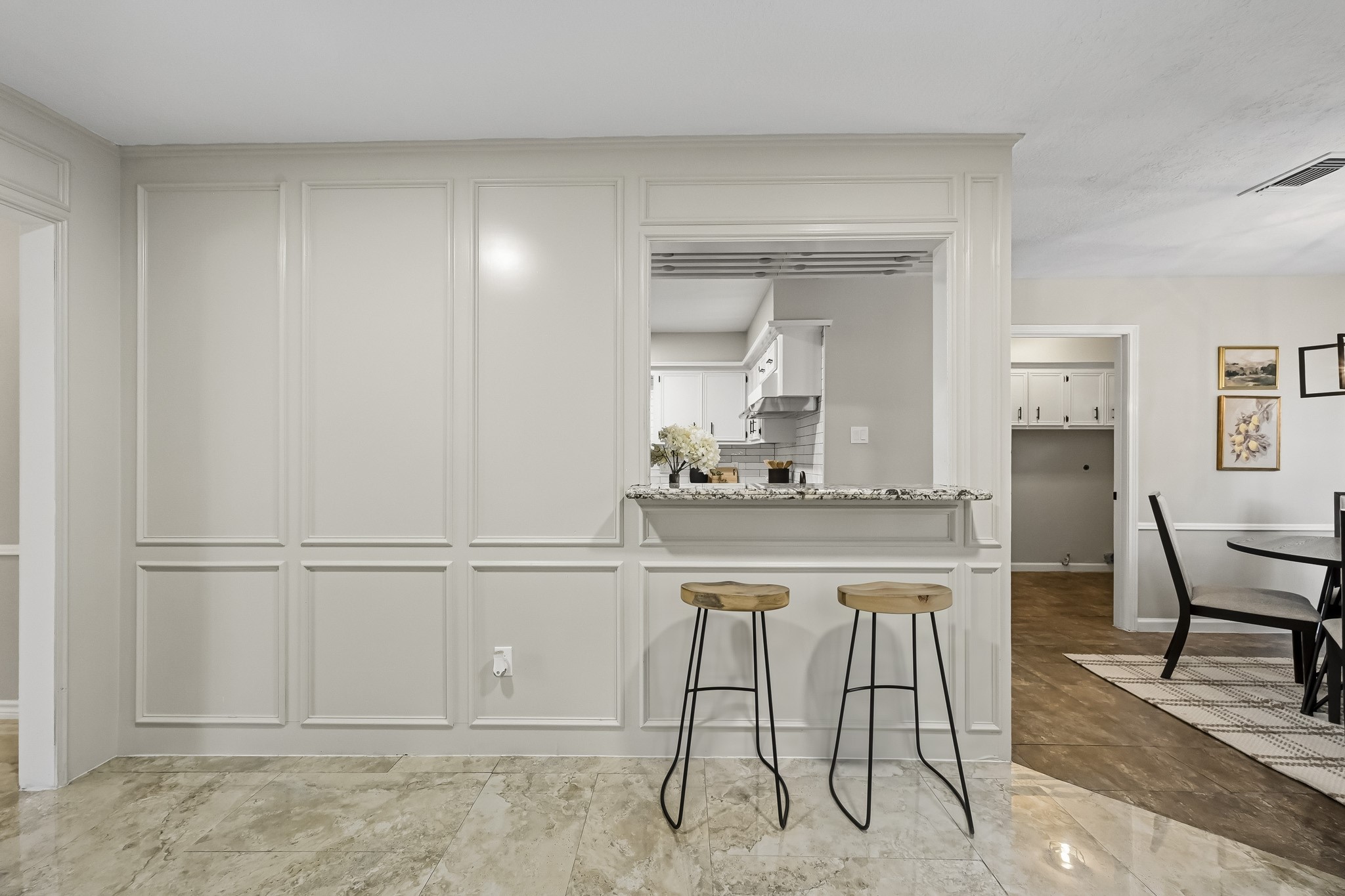 Elegant open-concept space featuring a chic breakfast bar with stylish stools, framed by classic paneling and leading to a bright kitchen area.