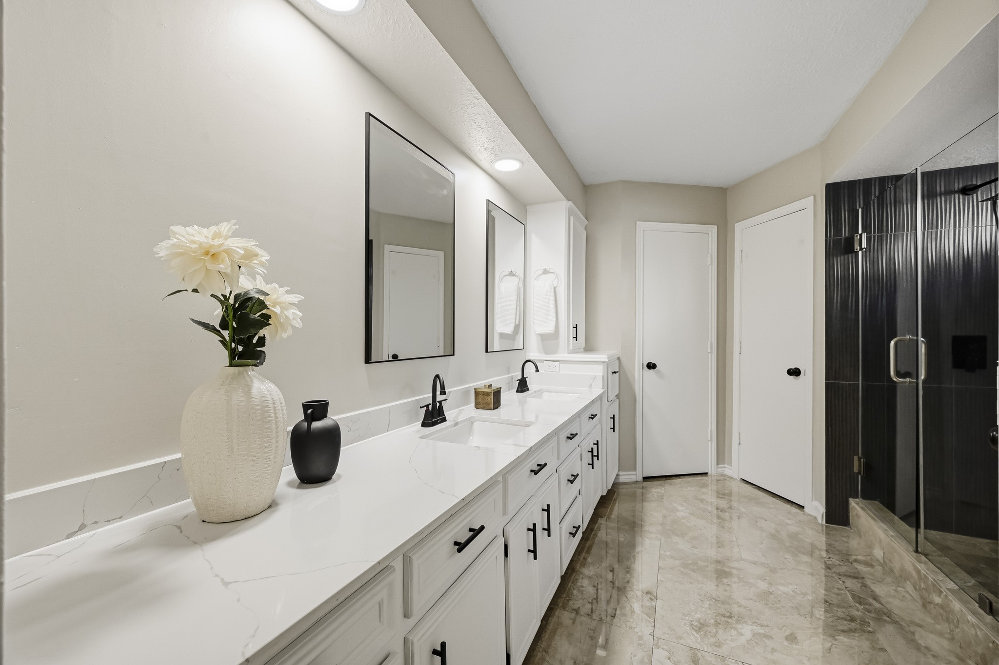 Elegant bathroom featuring a double vanity with sleek black fixtures, large mirrors, and a spacious glass-enclosed shower, all set against sophisticated tile flooring.