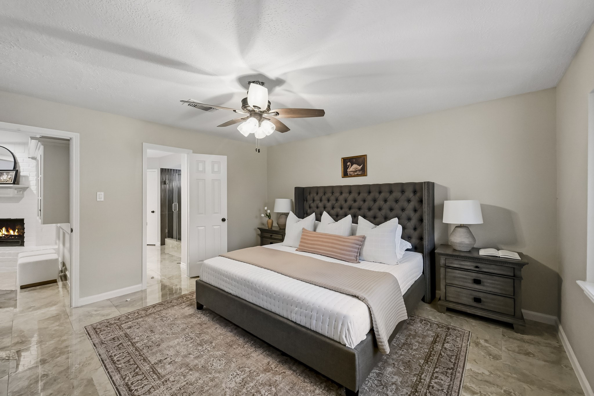 Spacious bedroom featuring a luxurious bed with a tufted headboard, elegant nightstands, and a cozy ambiance enhanced by a ceiling fan.