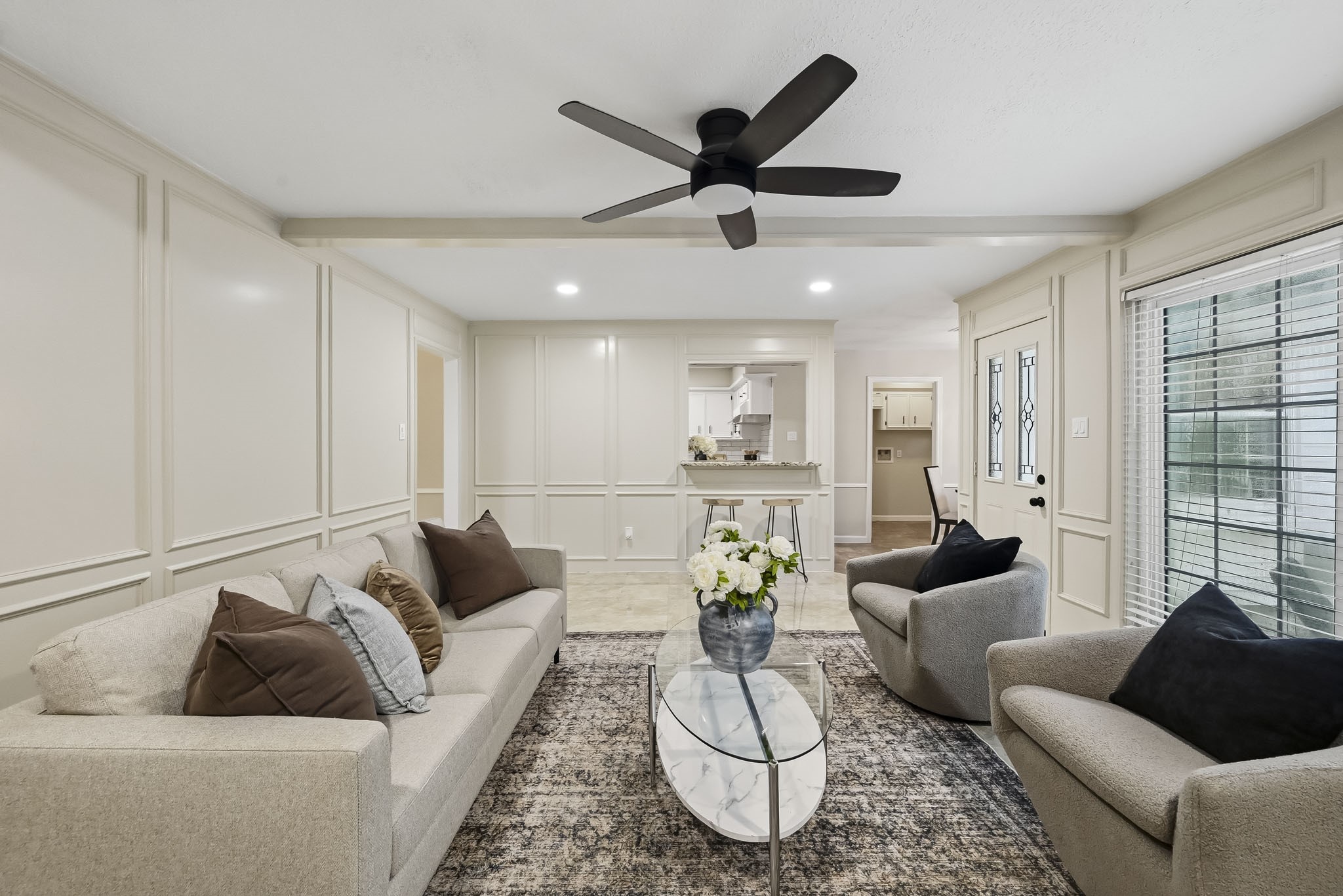 Elegant living area with neutral tones, featuring a cozy seating arrangement, modern ceiling fan, and large windows for natural light.