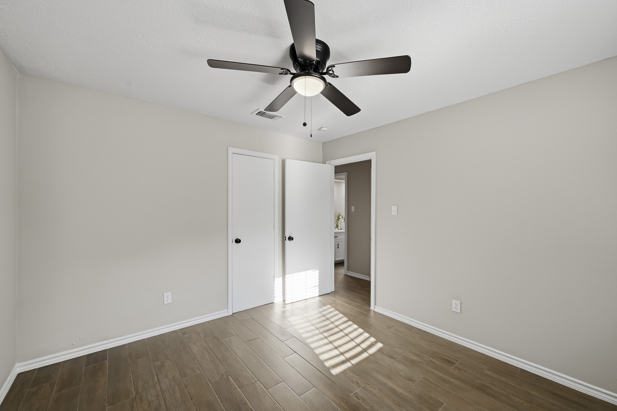 Bright and inviting room featuring elegant wood flooring, a modern ceiling fan, and neutral wall tones, offering a versatile space for any decor style.
