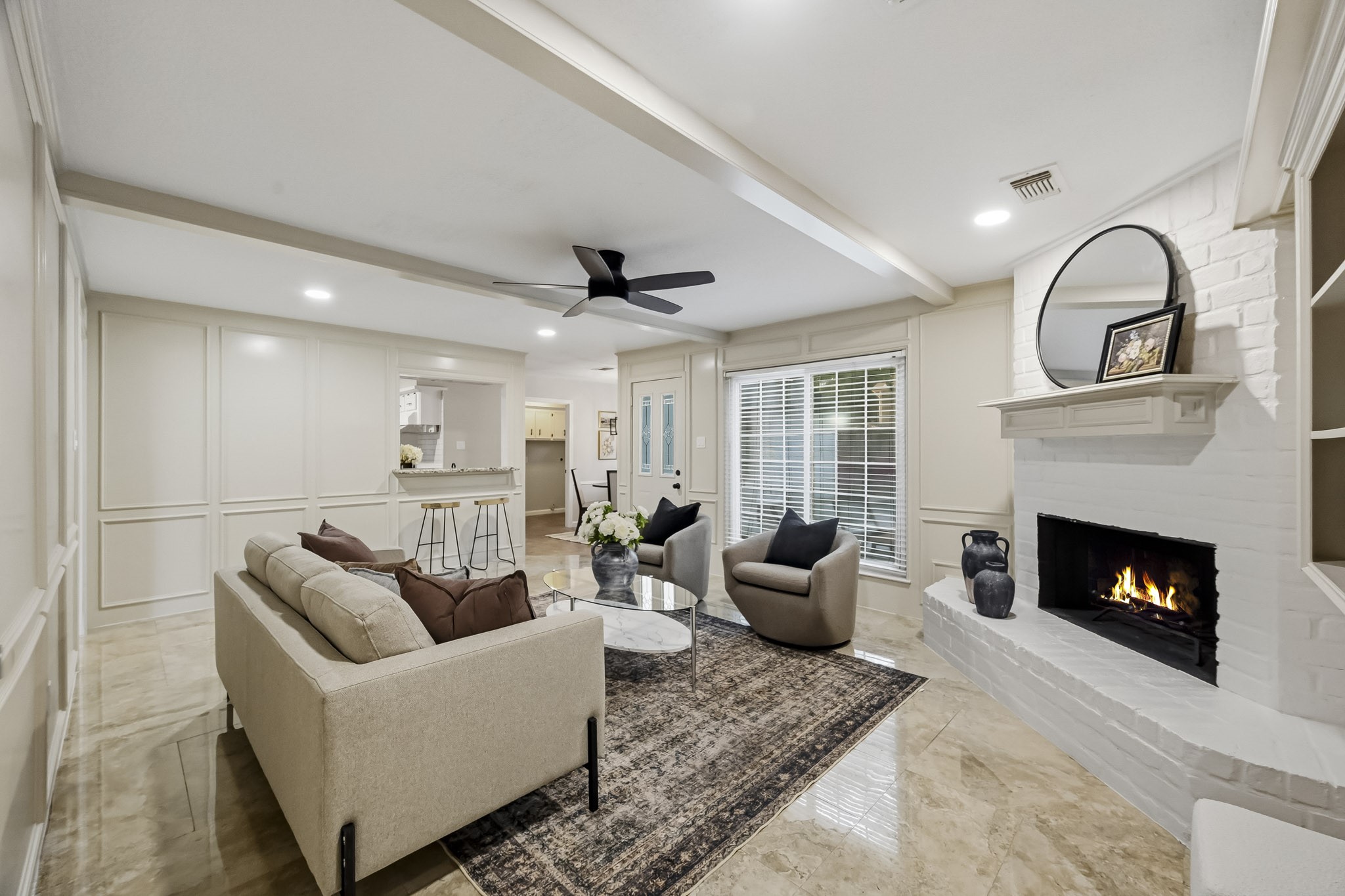 Inviting living room with a cozy fireplace, elegant ceiling beams, and ample natural light from large windows.