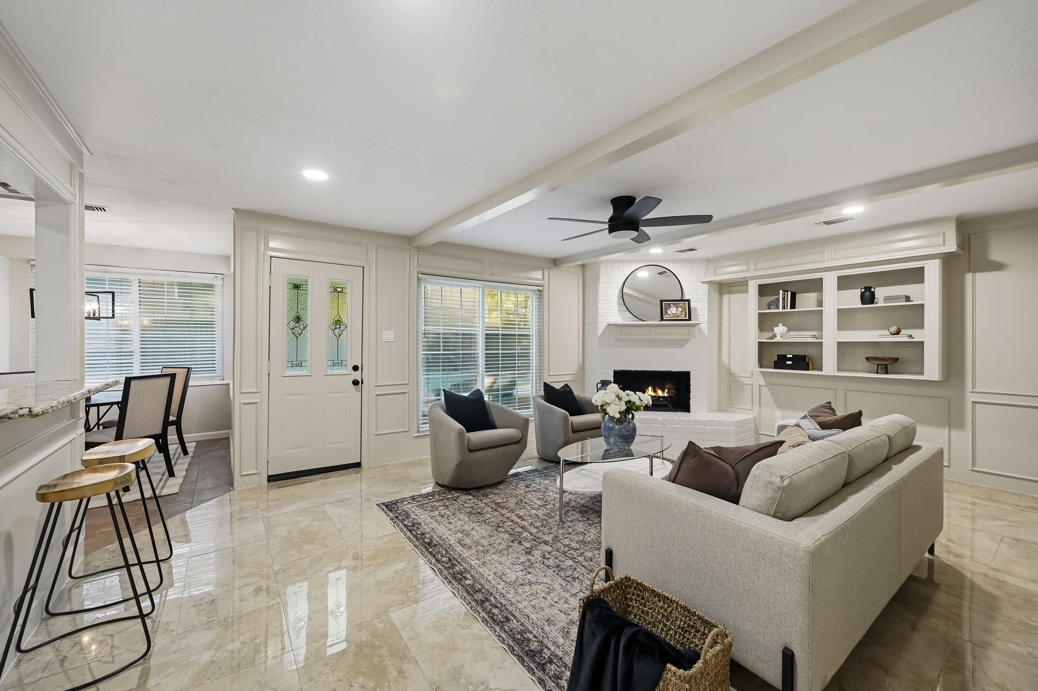 Spacious living area with elegant marble floors, a cozy fireplace, and custom built-in shelving, seamlessly connected to a dining nook through a granite breakfast bar.