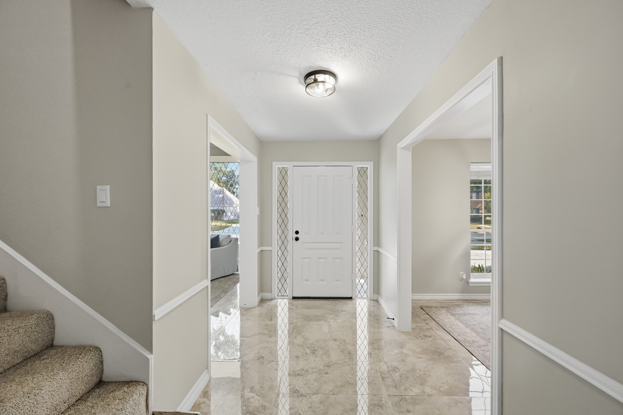 Bright and inviting entryway with glossy tile flooring and neutral walls, flanked by open doorways leading to spacious living areas, offering a warm welcome to your home.