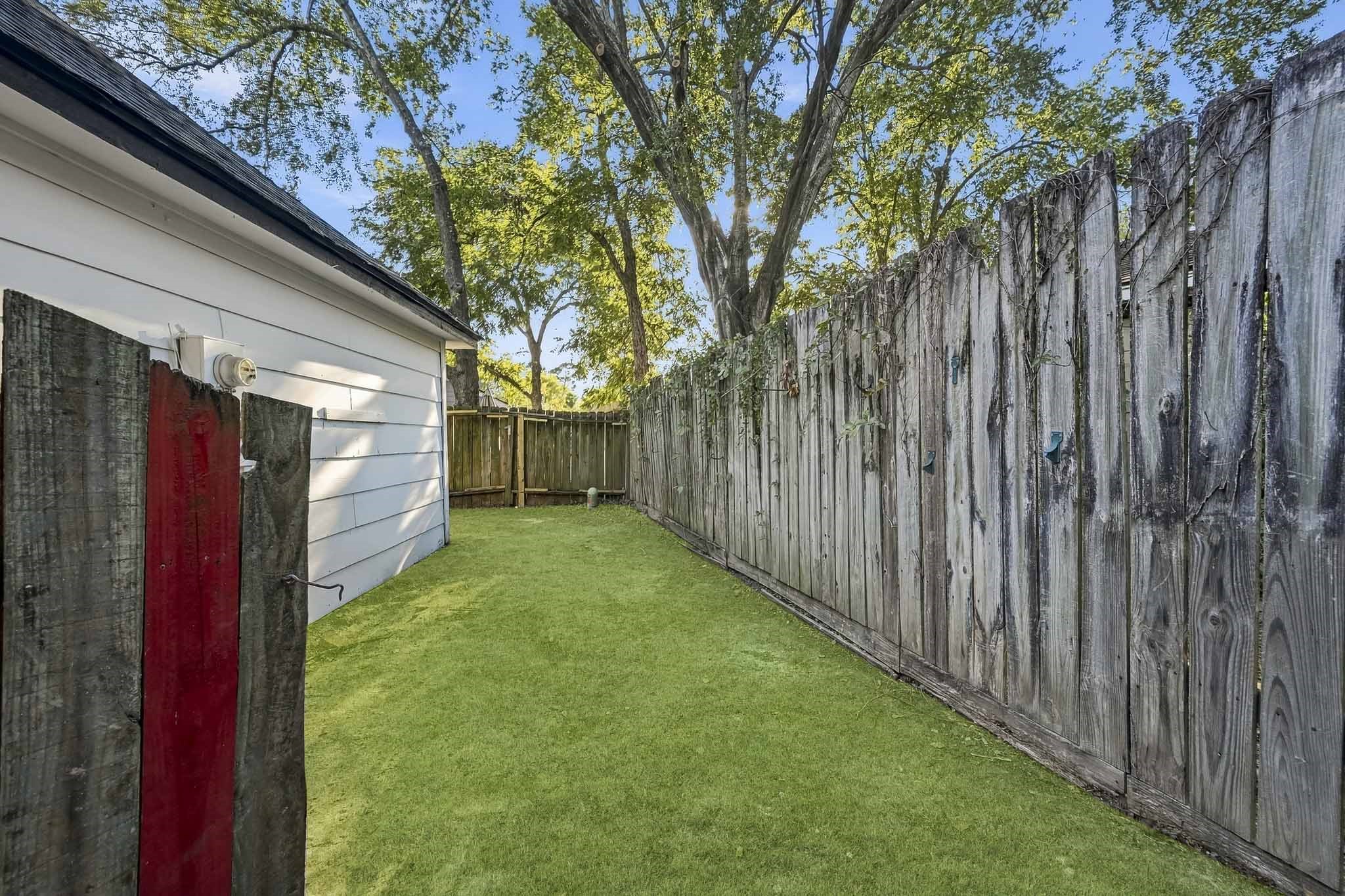 Charming backyard space with lush green lawn, bordered by a classic wooden fence, perfect for outdoor relaxation or gardening.