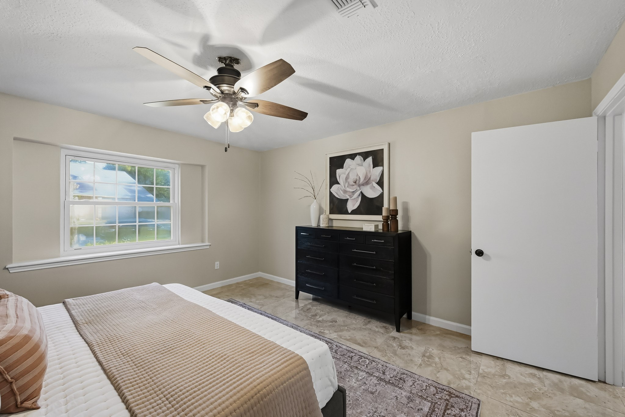 Cozy bedroom featuring a large window that fills the space with natural light, complemented by neutral walls and a ceiling fan for comfort.