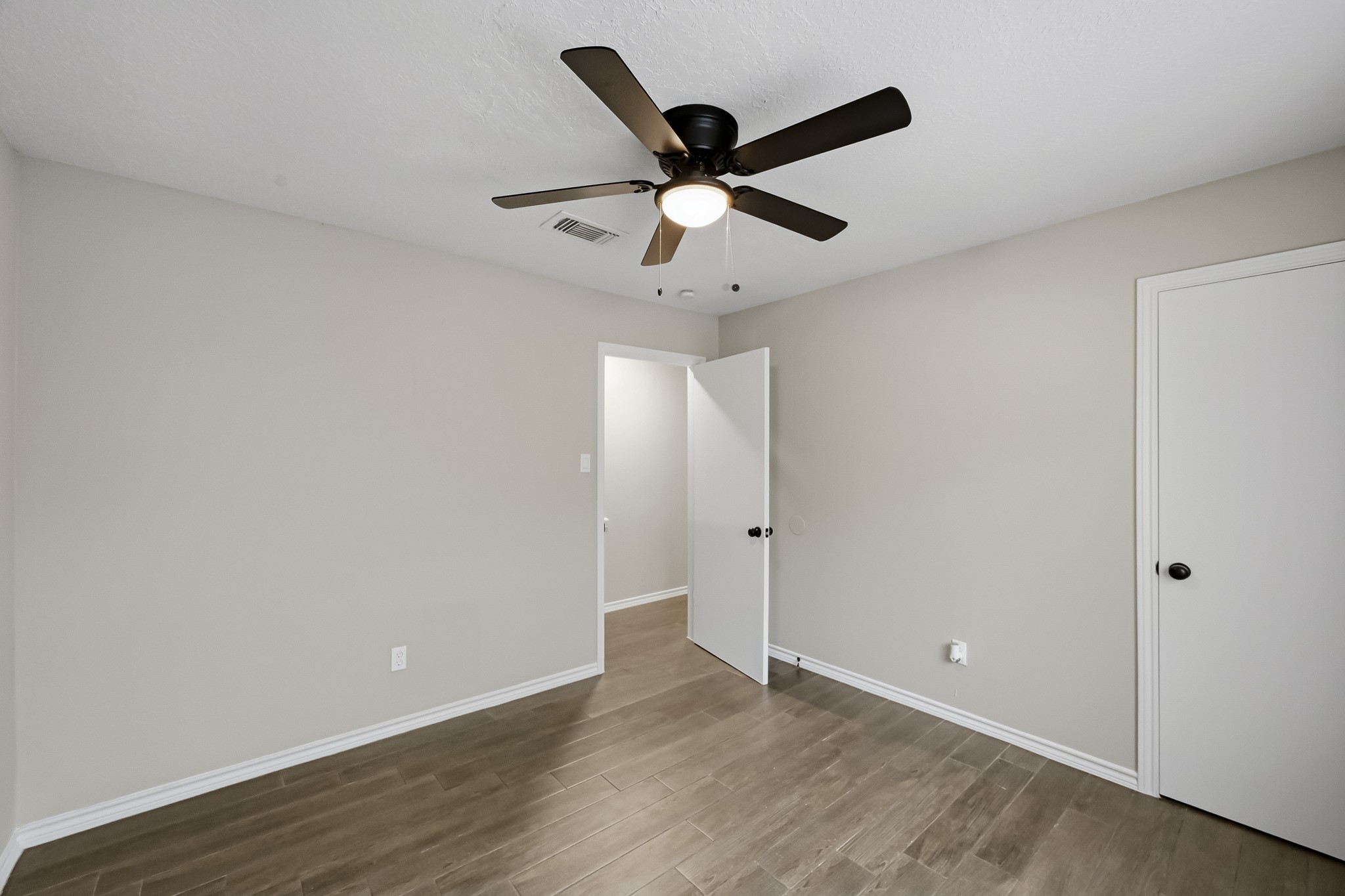 Bright and inviting bedroom featuring sleek wooden floors, a modern ceiling fan, and neutral walls for a serene atmosphere.