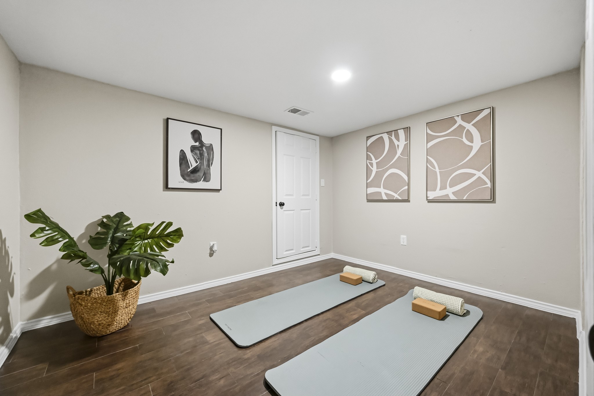 Cozy and inviting exercise room featuring elegant wood flooring, soft lighting, and stylish wall art, perfect for yoga or meditation.