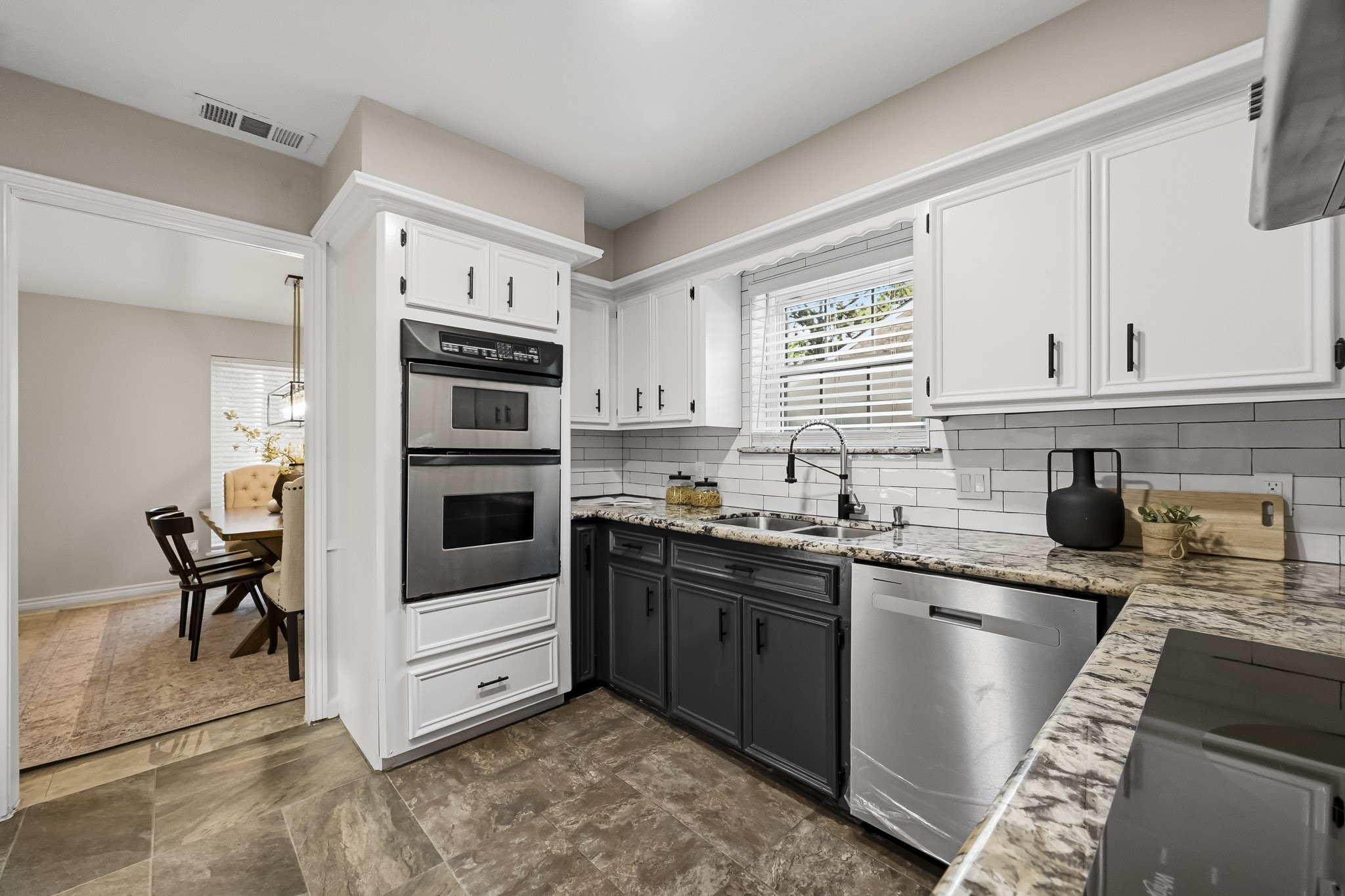 Stylish kitchen with modern stainless steel appliances, dual-tone cabinetry, and granite countertops, seamlessly leading to a cozy dining area.